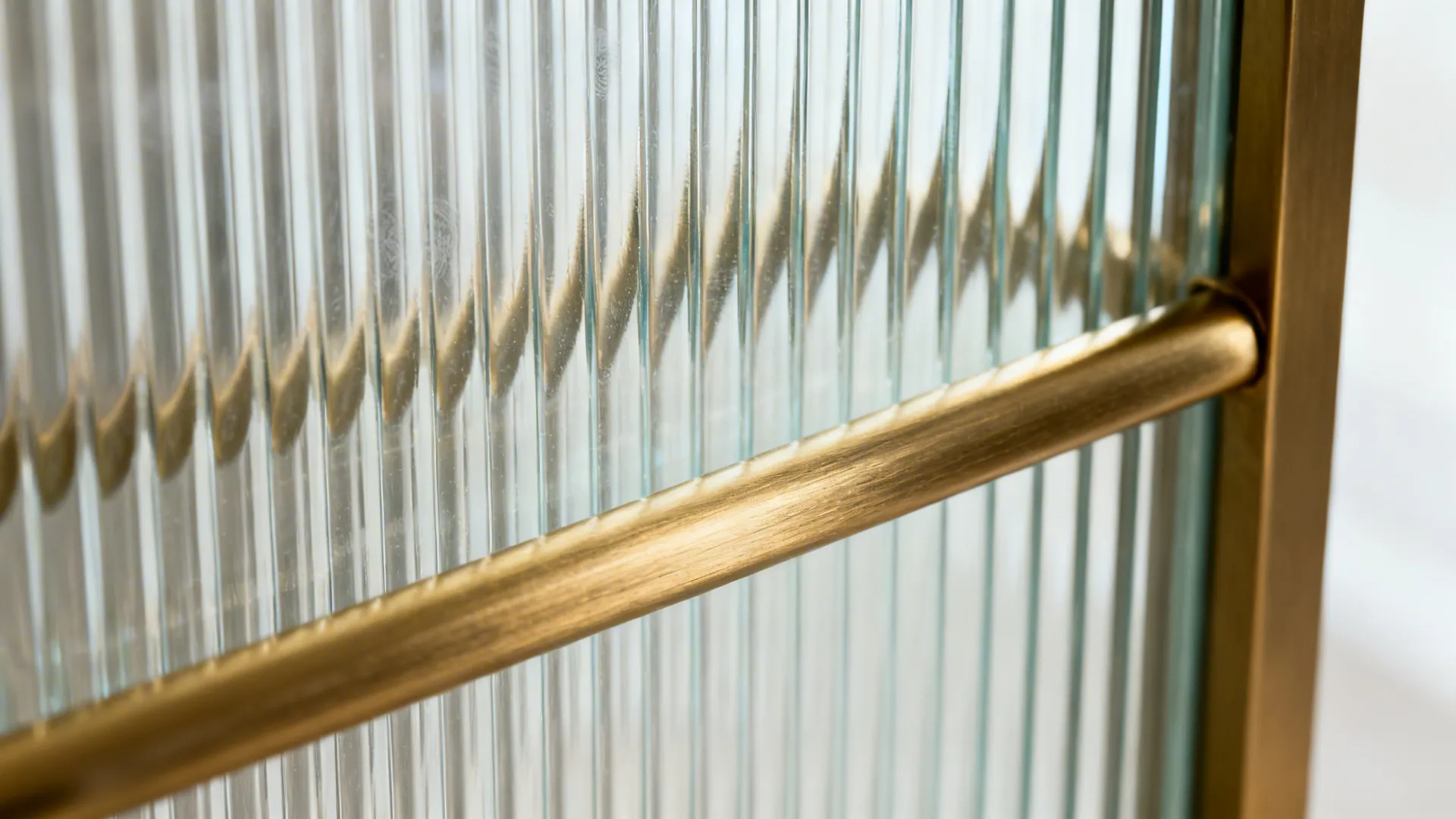 Macro of vertical reeded glass with soft light and a brushed brass rail.