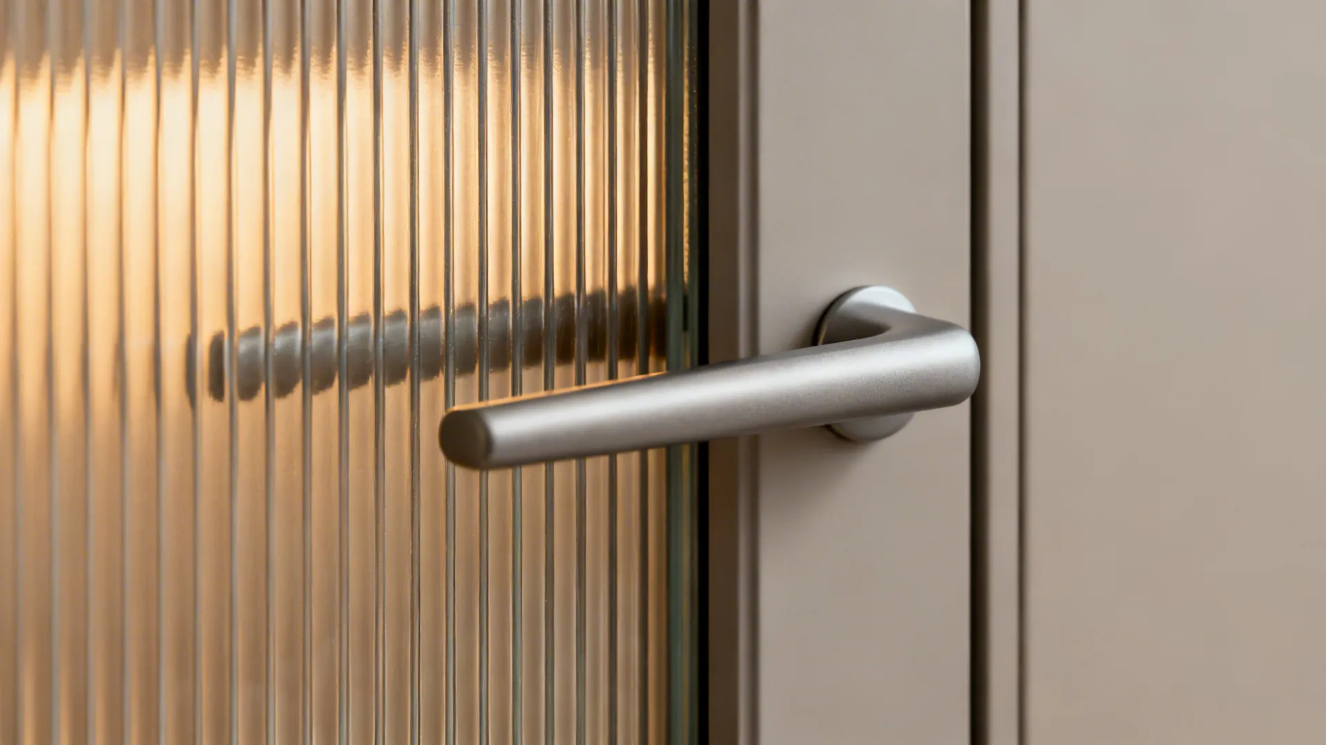 Macro detail of reeded glass texture next to a sleek aluminium pull handle under warm light.
