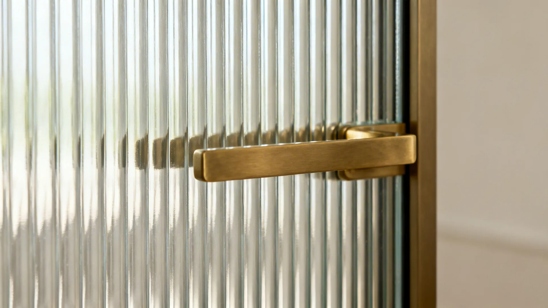 Close up of gold metal handle on textured glass door with vertical line patterns in sunlight