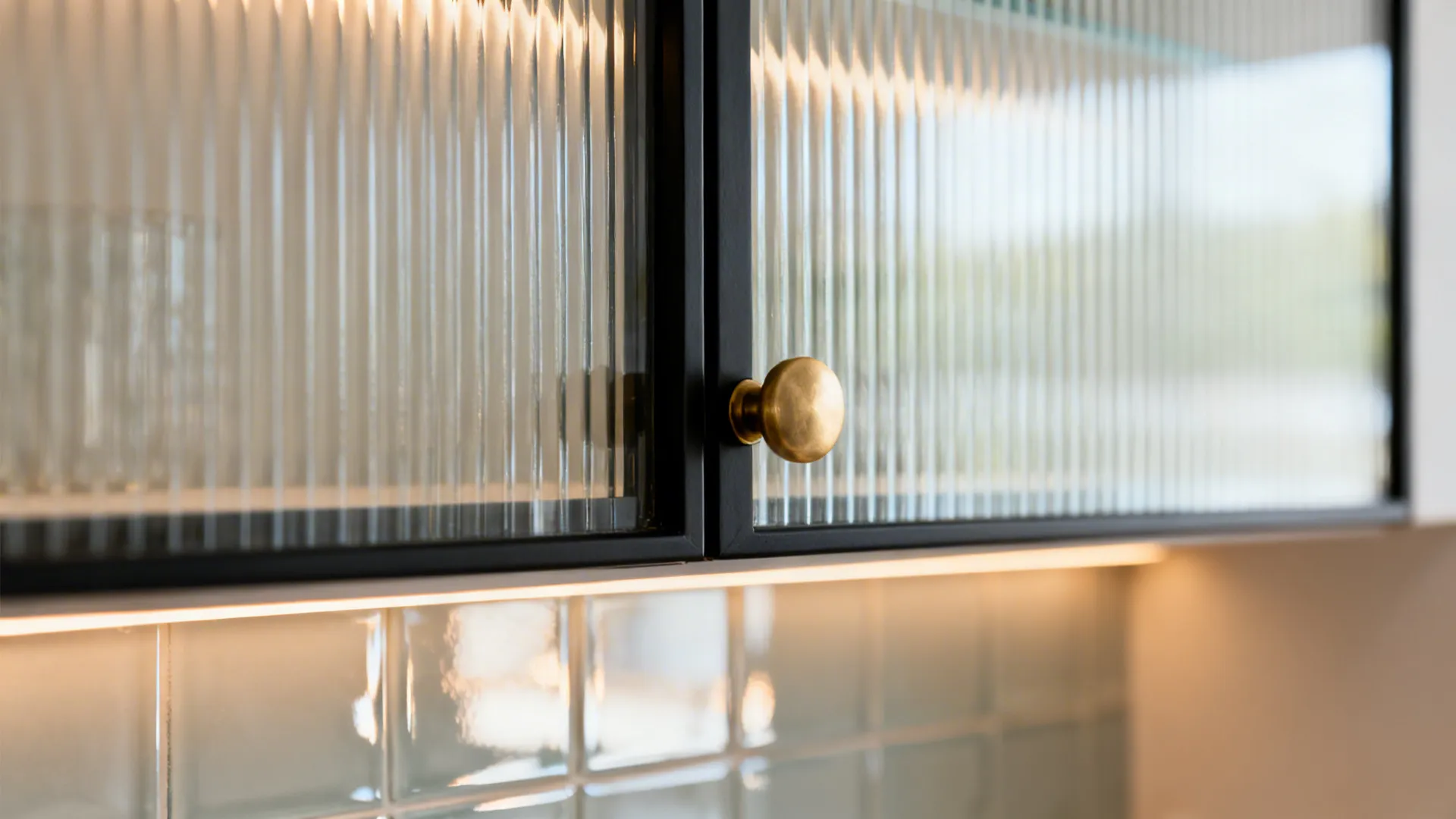 Macro of reeded glass door with warm shelf lighting and slim black frame.