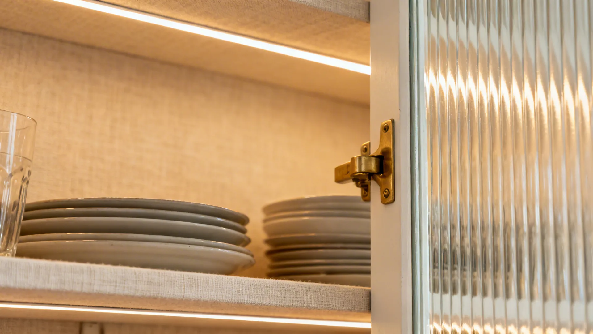 Macro of reeded glass door with warm LED glow revealing softly blurred tableware.