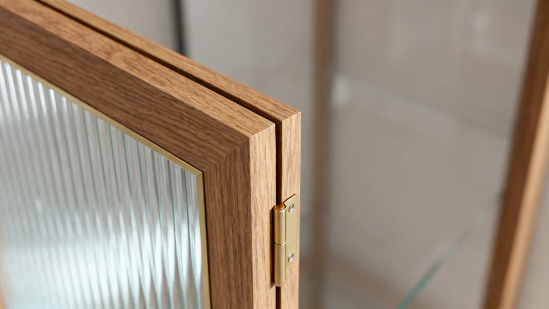 Close-up of an oak-framed reeded glass door with fine joinery and brass hinge.