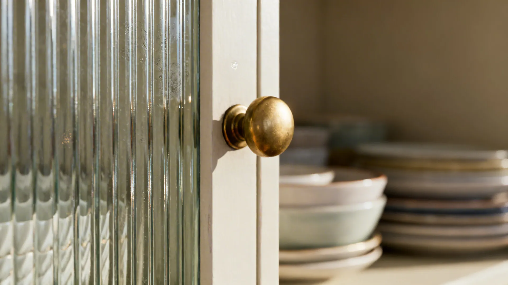 Macro of vertical reeded glass door with matte brass knob and soft reflections.