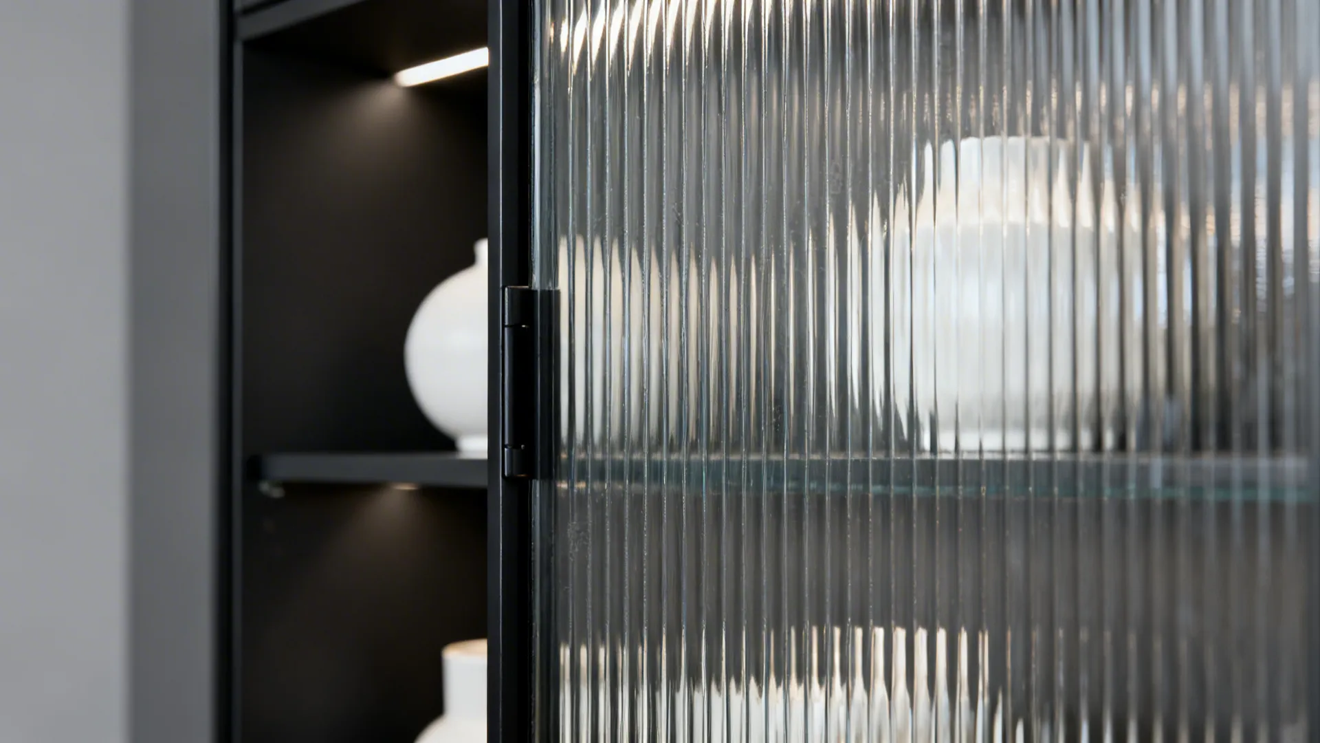 Macro of reeded glass cabinet door with slim matte black frame and soft light.