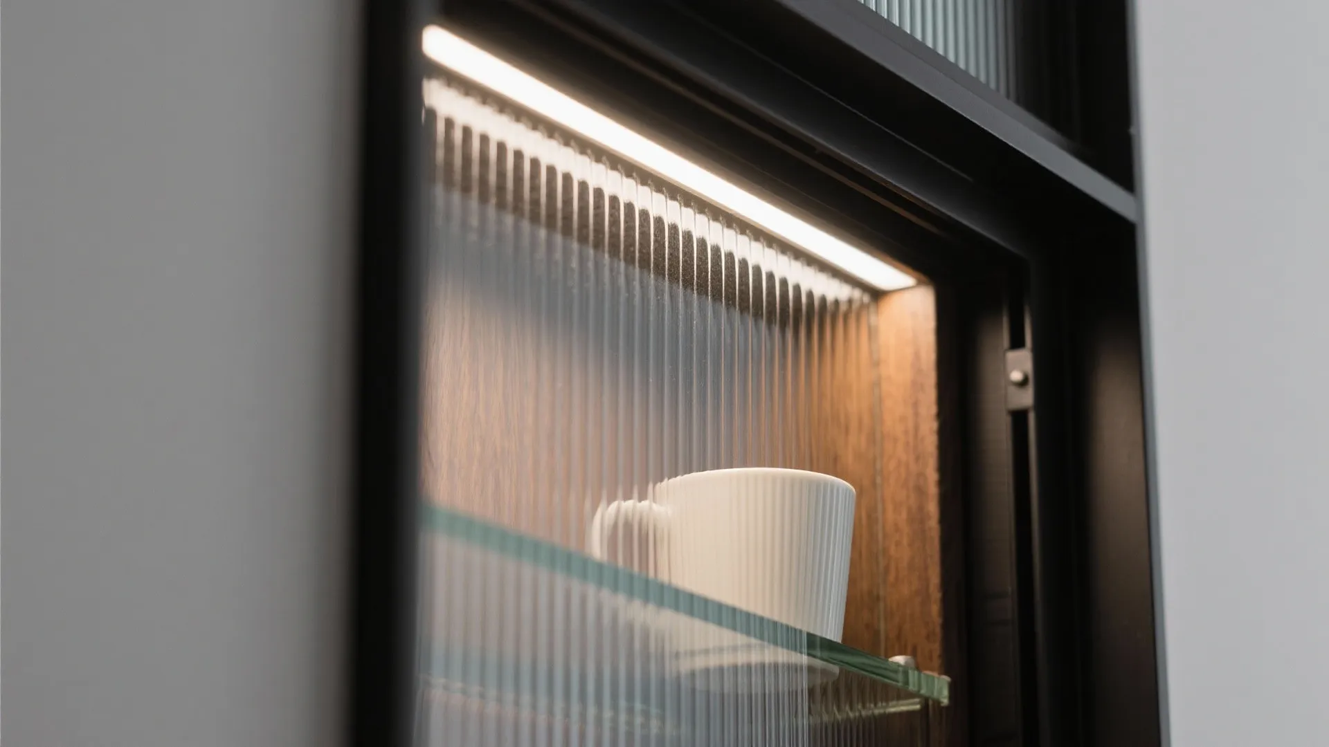 Close up of a glass cabinet with lighting inside showing a white cup on a shelf