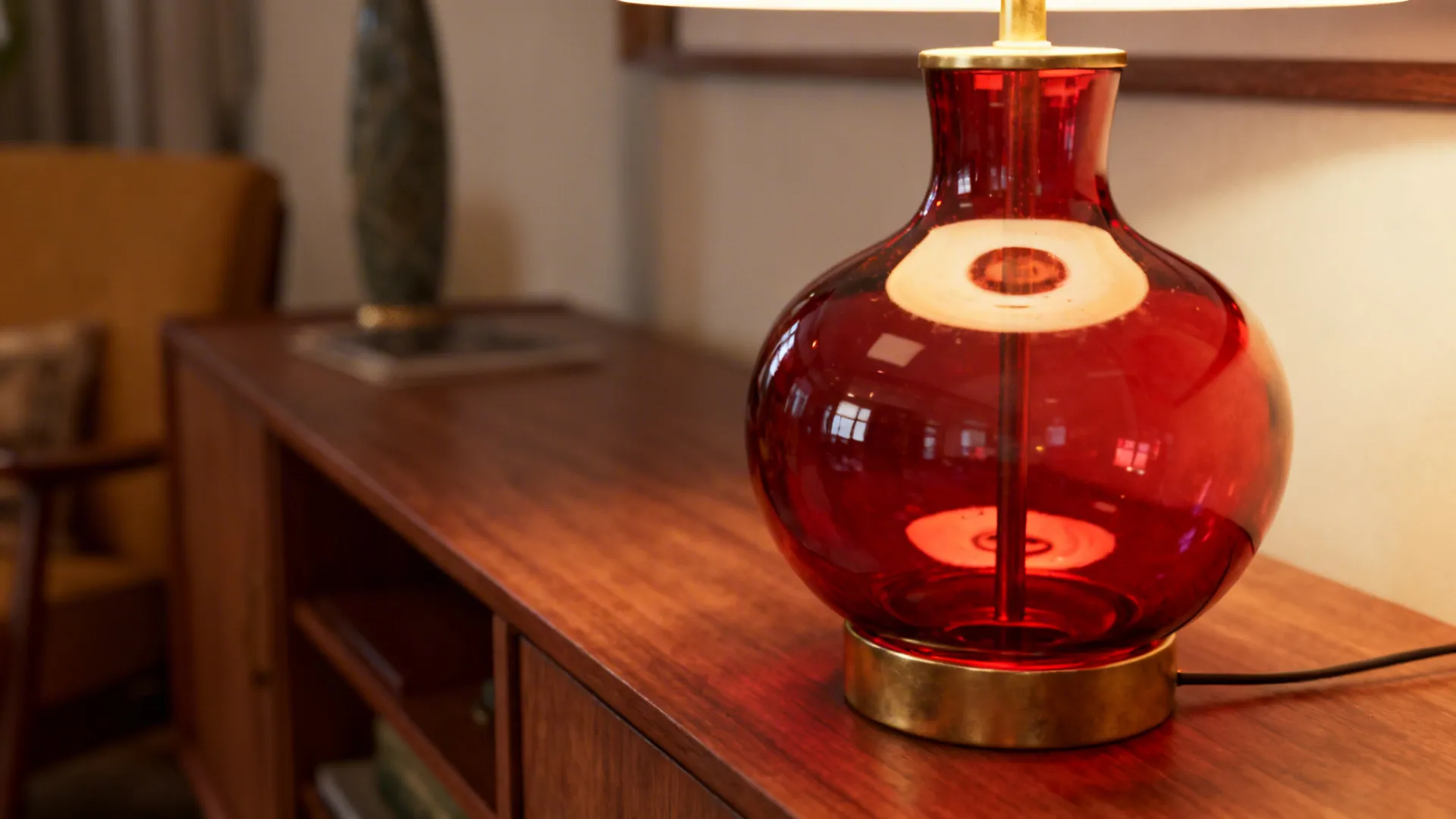 Retro blown red glass table lamp with brass accents on a mid-century sideboard.
