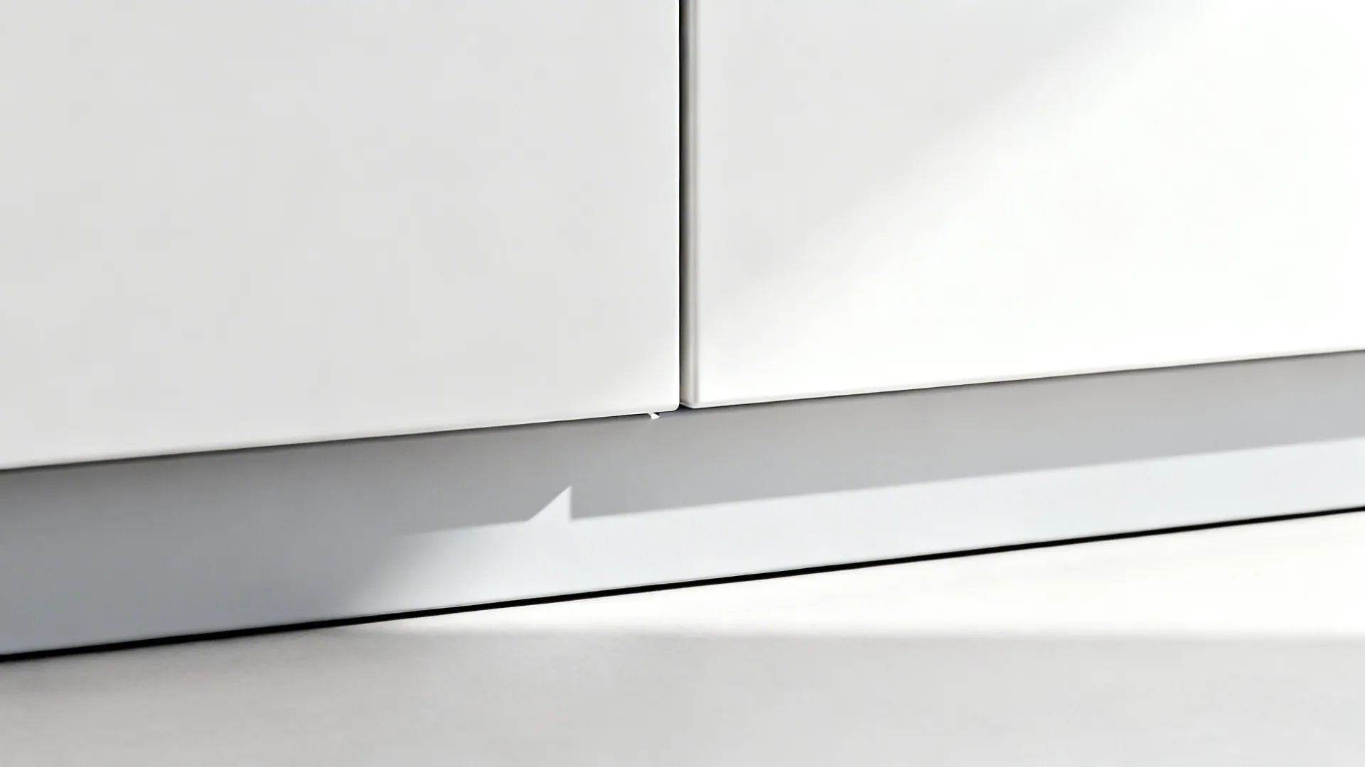 Macro of a 3 mm shadow gap and toe-kick on matte white minimalist cabinet fronts.