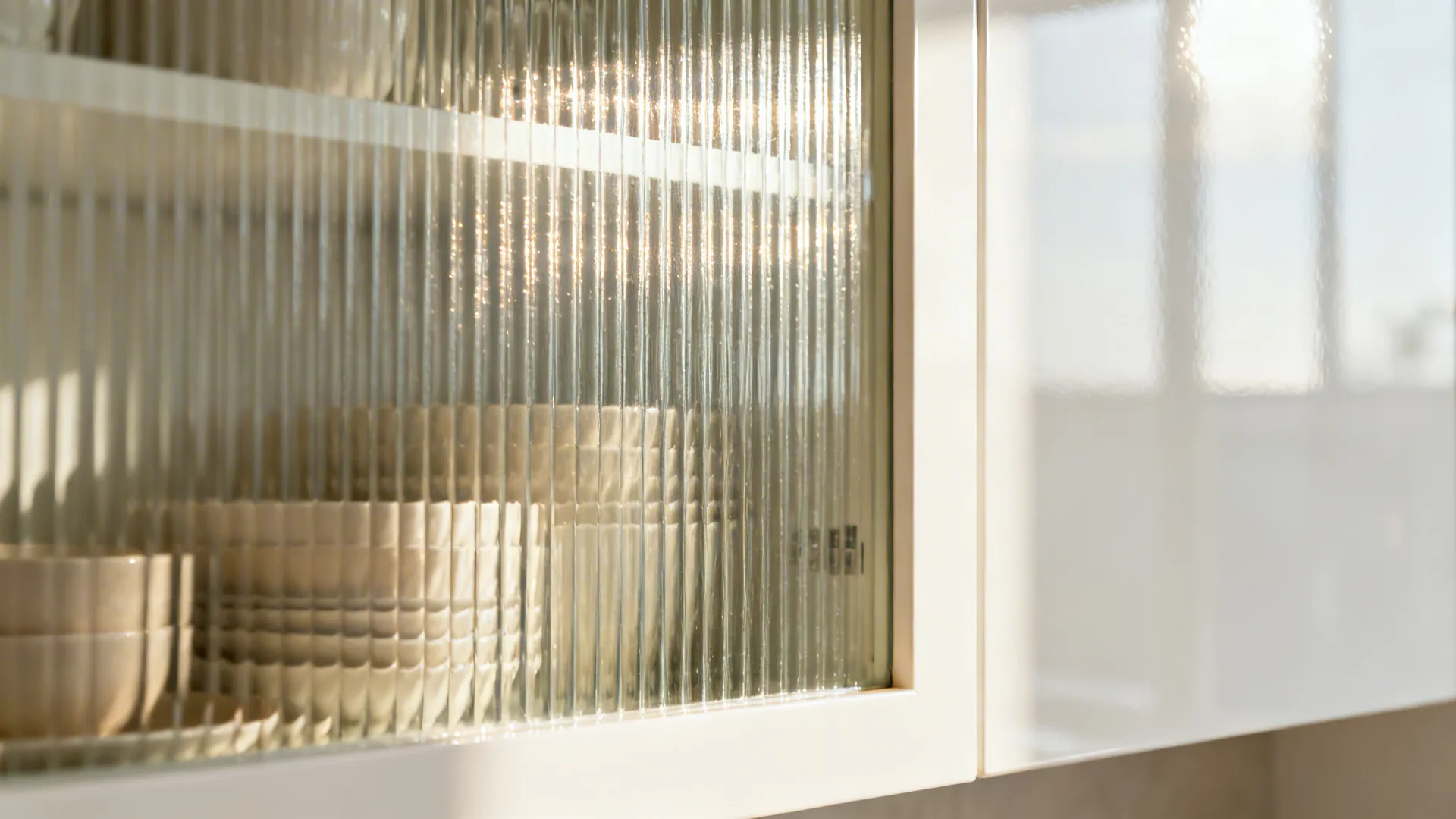 Close-up of ribbed glass cabinet door with soft reflections and a glossy white panel nearby.