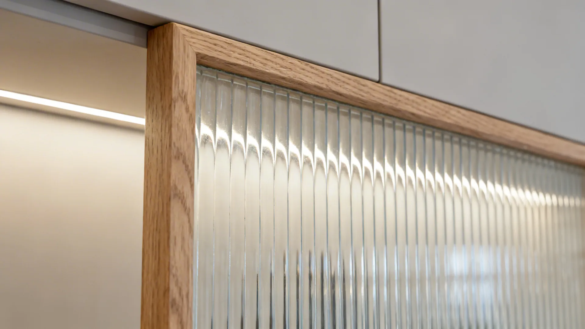 Close up of textured glass cabinet door with light wood frame and warm light fixture