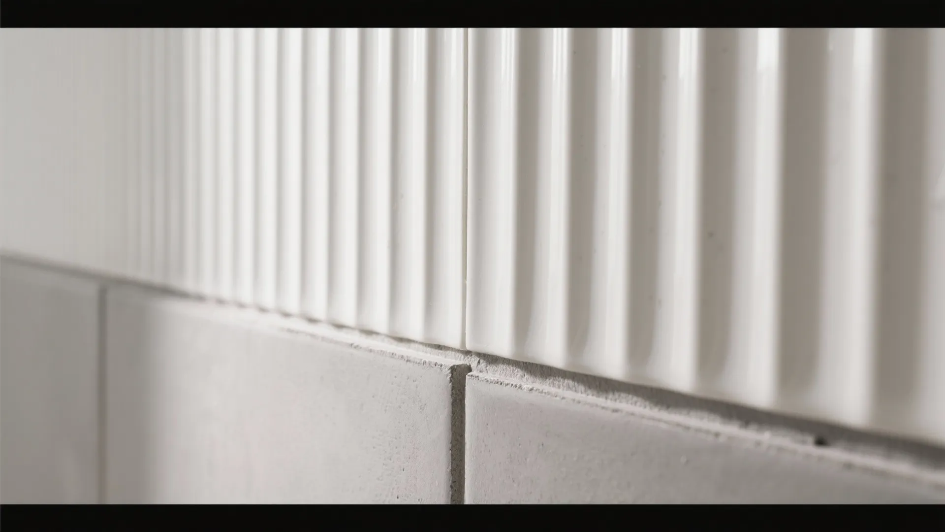 Macro detail of white ribbed ceramic tile meeting matte grey cement-look porcelain.