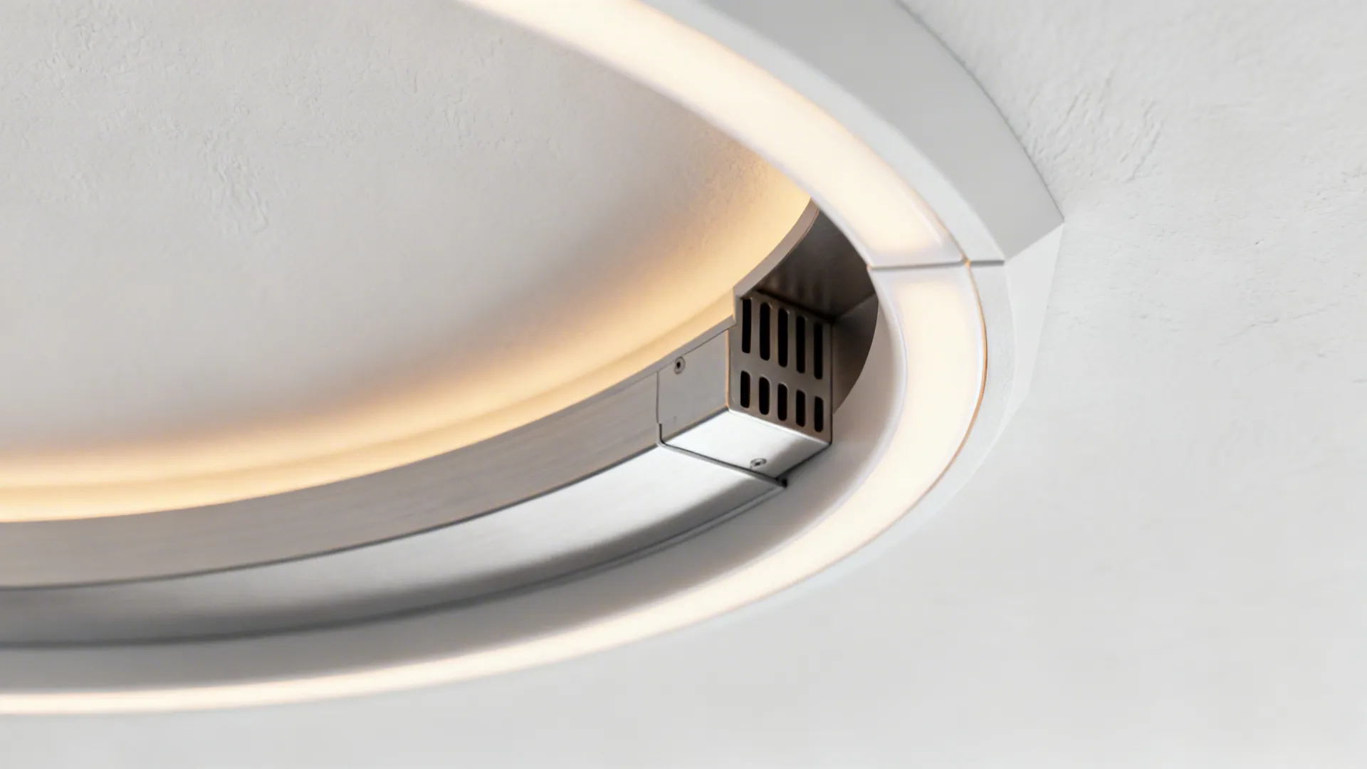 Close up of a round white light fixture on a ceiling showing the internal metal parts