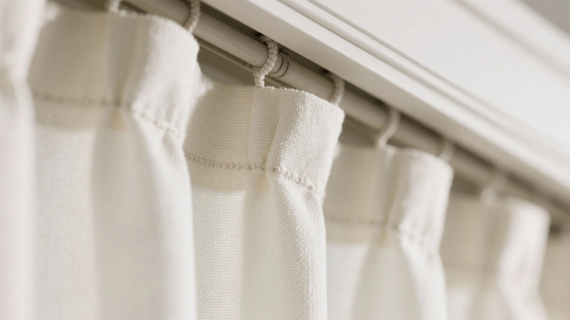 Close up view of white fabric curtain hanging on a metal rod in a bright room
