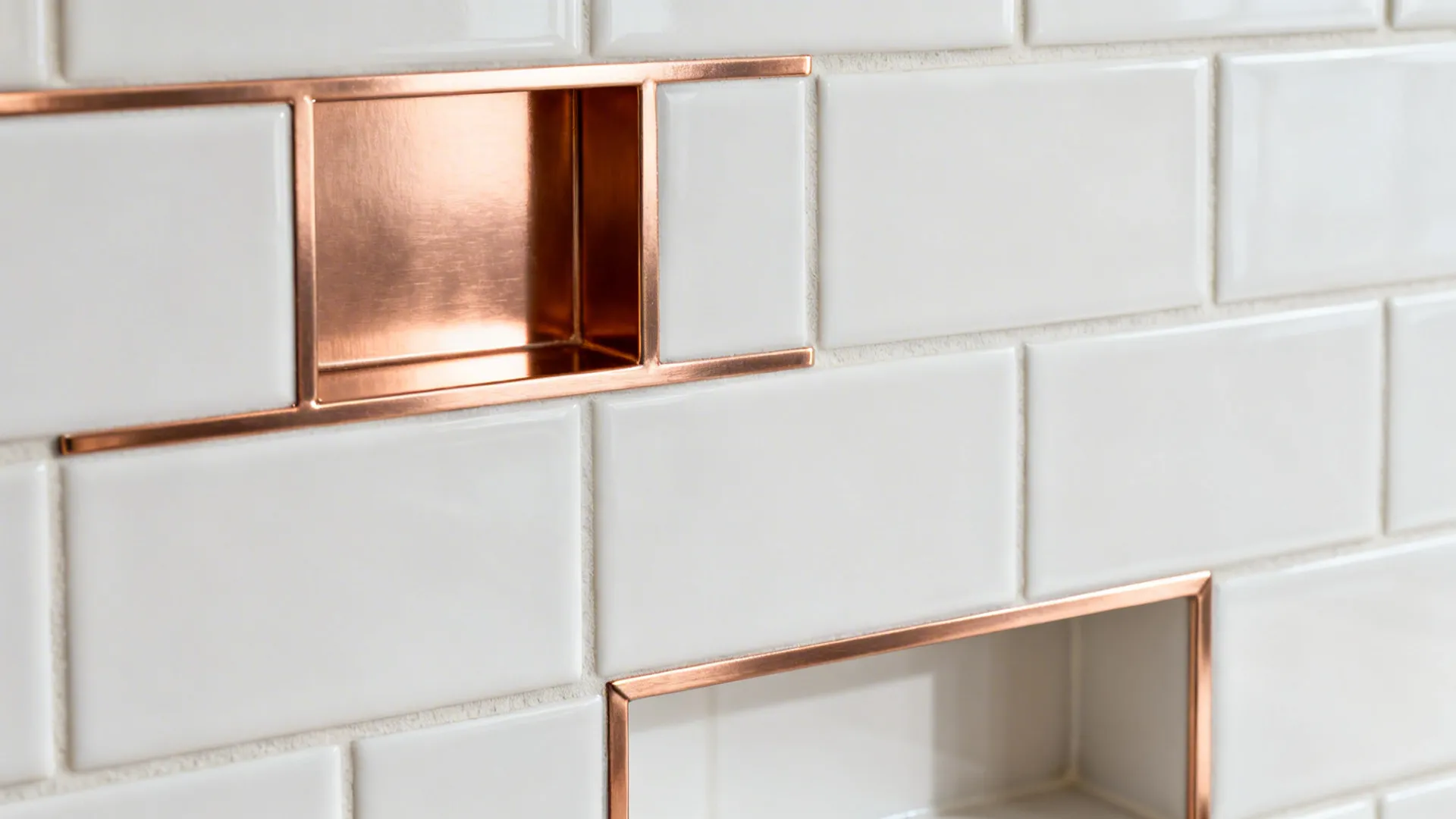 Macro of slim brushed rose gold liner trim accenting a matte white tile backsplash.