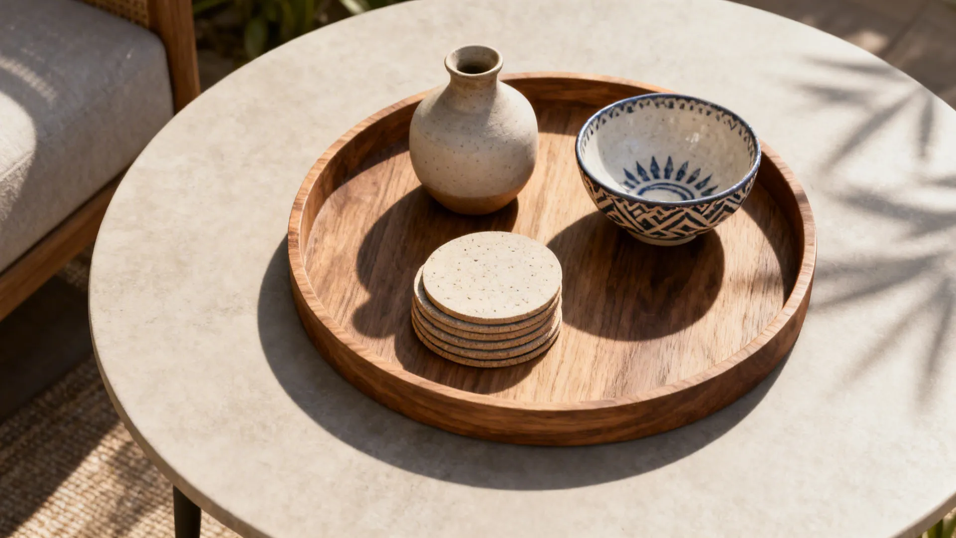 Top-down view of a round tray with a small vase, coasters and a decorative bowl on a round table.