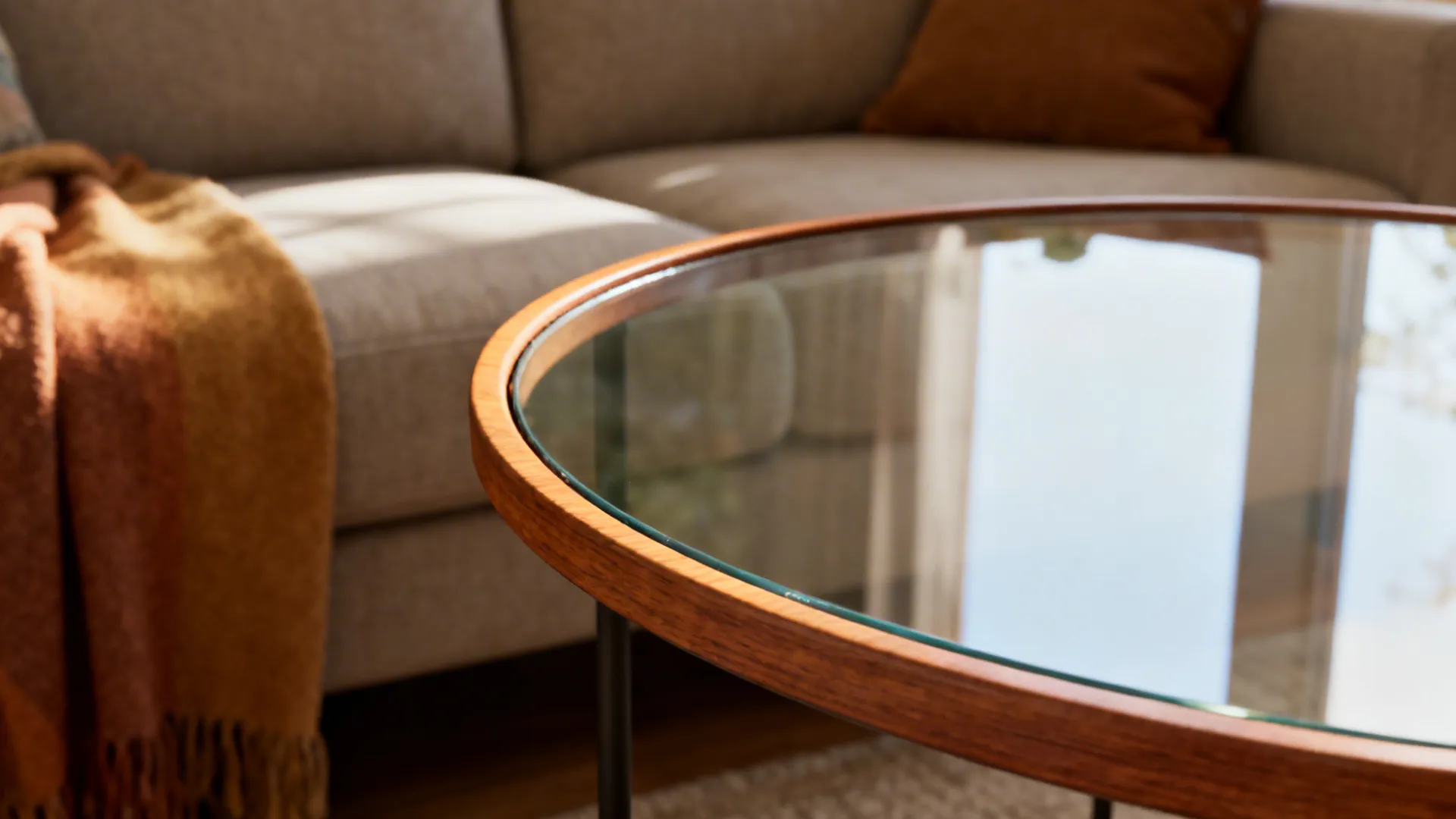Rounded glass end table with a thin wooden rim next to a sofa, showing wood grain detail.