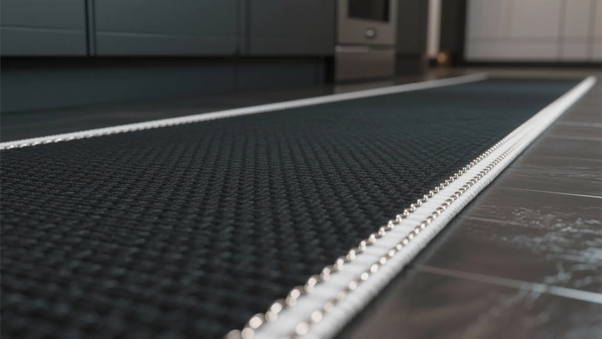 Close up shot of a black kitchen rug with white border detail on dark floor