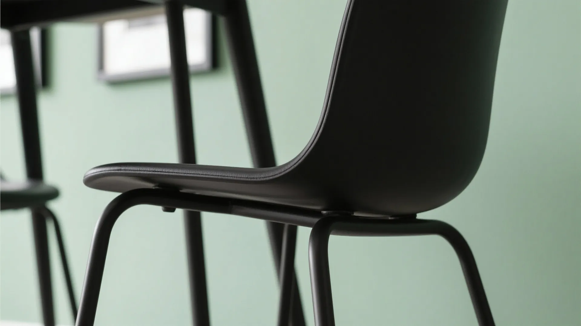 Close up view of black chair with metal legs against a light green painted wall