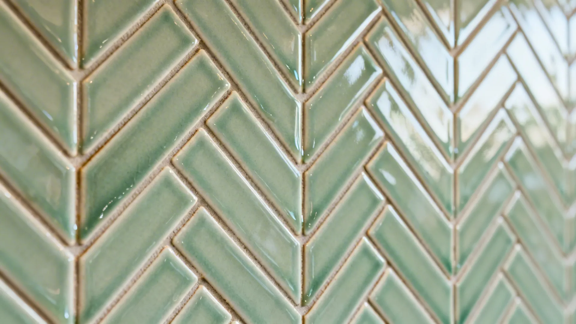 Macro of soft sage glazed ceramic herringbone backsplash with clean grout lines.