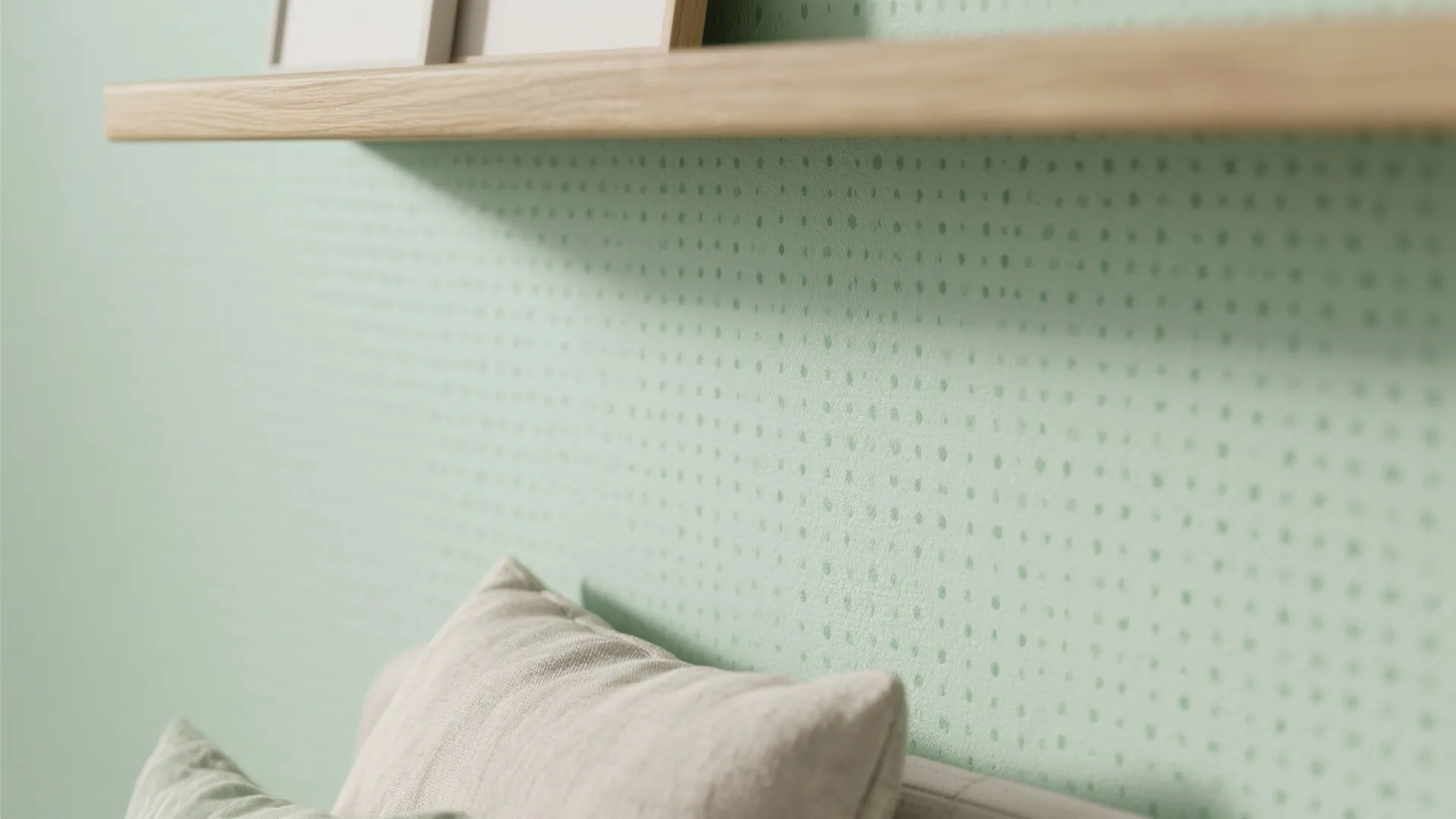 Close up of light green wallpaper with small dot pattern behind a wooden shelf and pillow