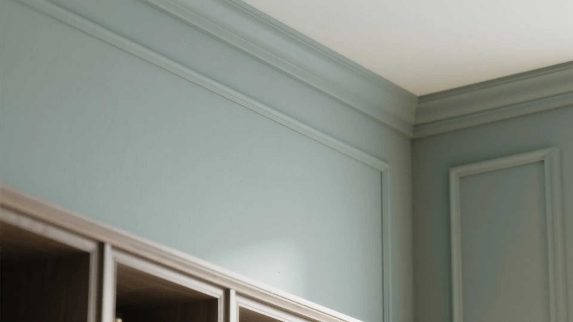 Close up showing light green wall panel details with ceiling trim and top wood cabinet