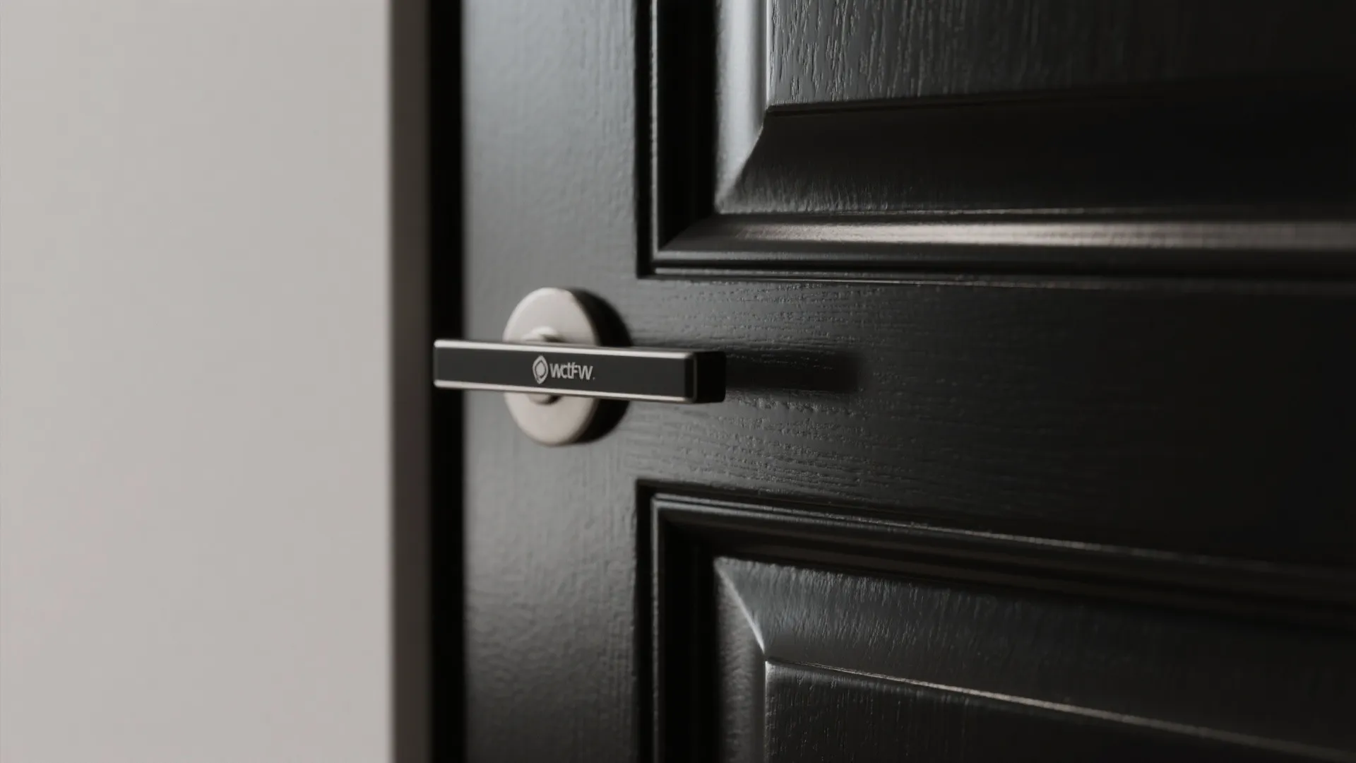 Close up of a black cabinet door featuring a silver handle and a wall panel