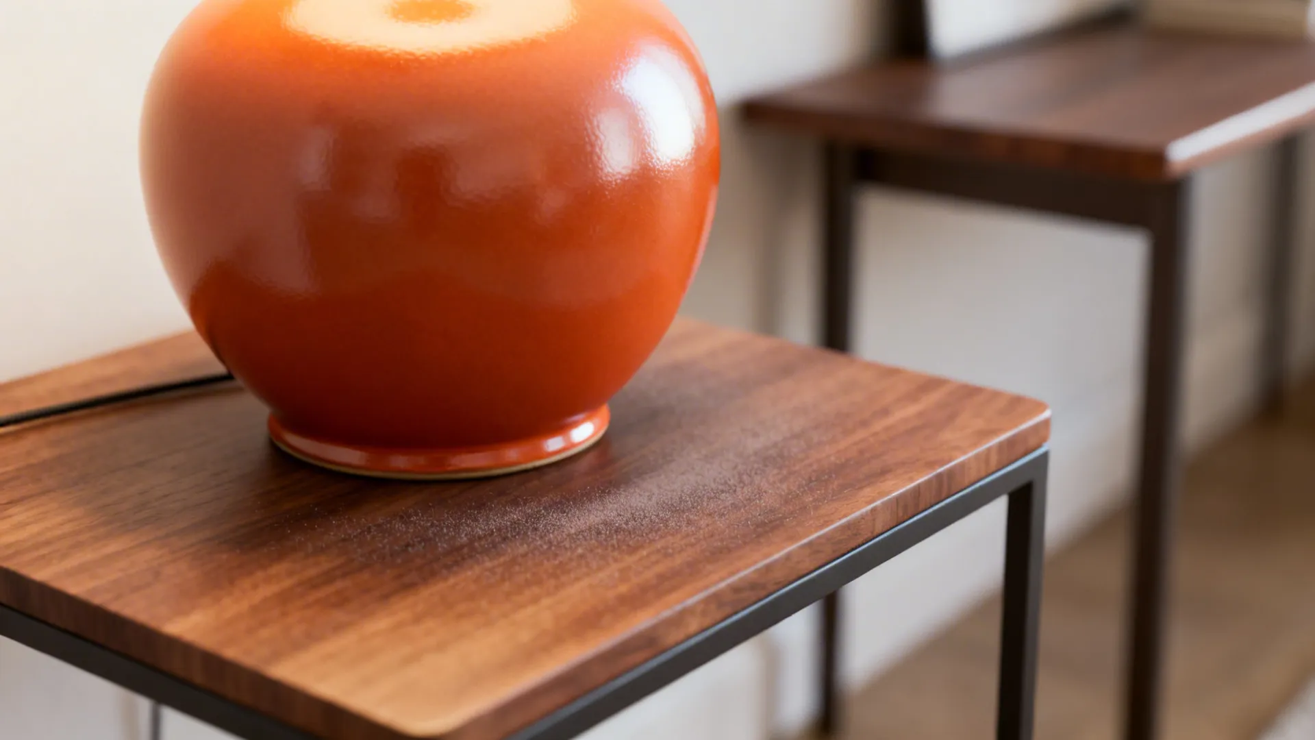 Macro view of a satin orange ceramic lamp base on a compact side table showing warm sheen and texture.