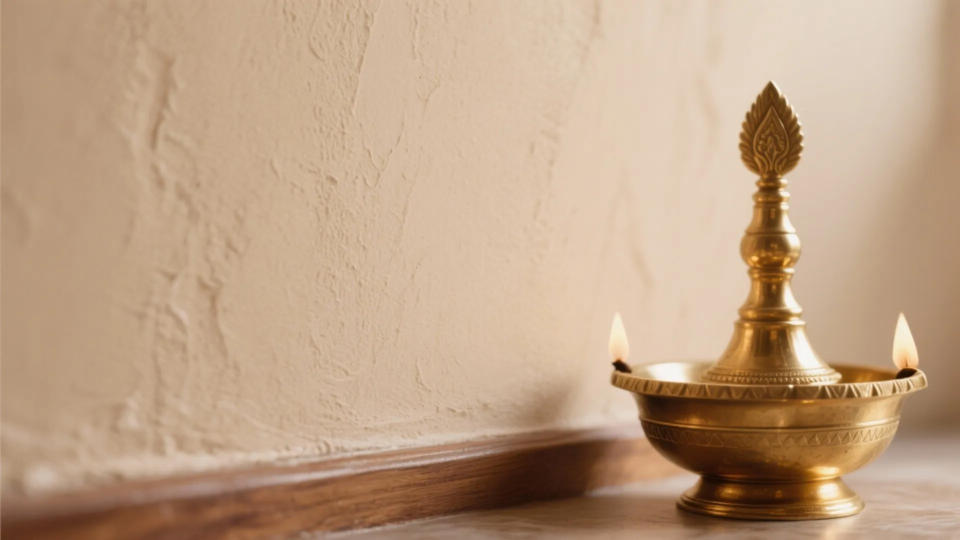 Macro of satin clay beige wall beside a brass diya with soft reflection.