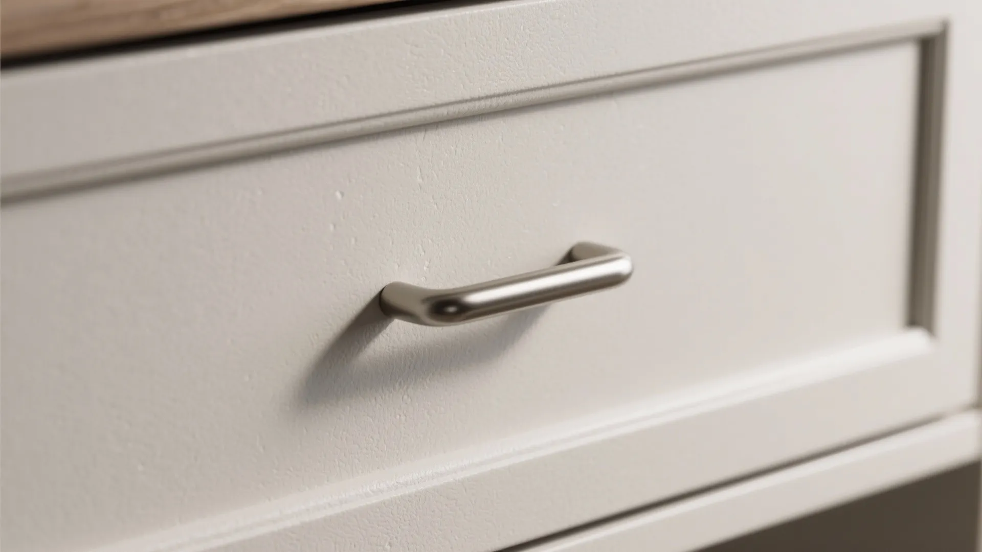 Close up view of a small metal handle installed on a white kitchen cabinet drawer
