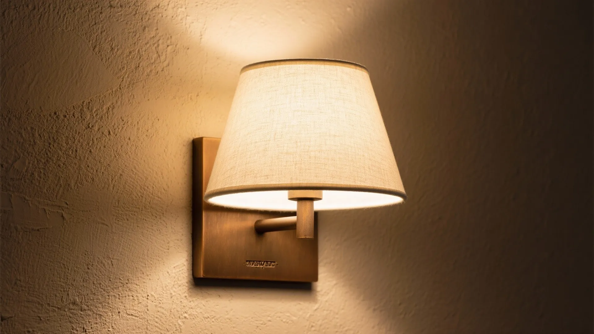 Small wall light with a beige fabric shade mounted on a rough beige interior bedroom wall