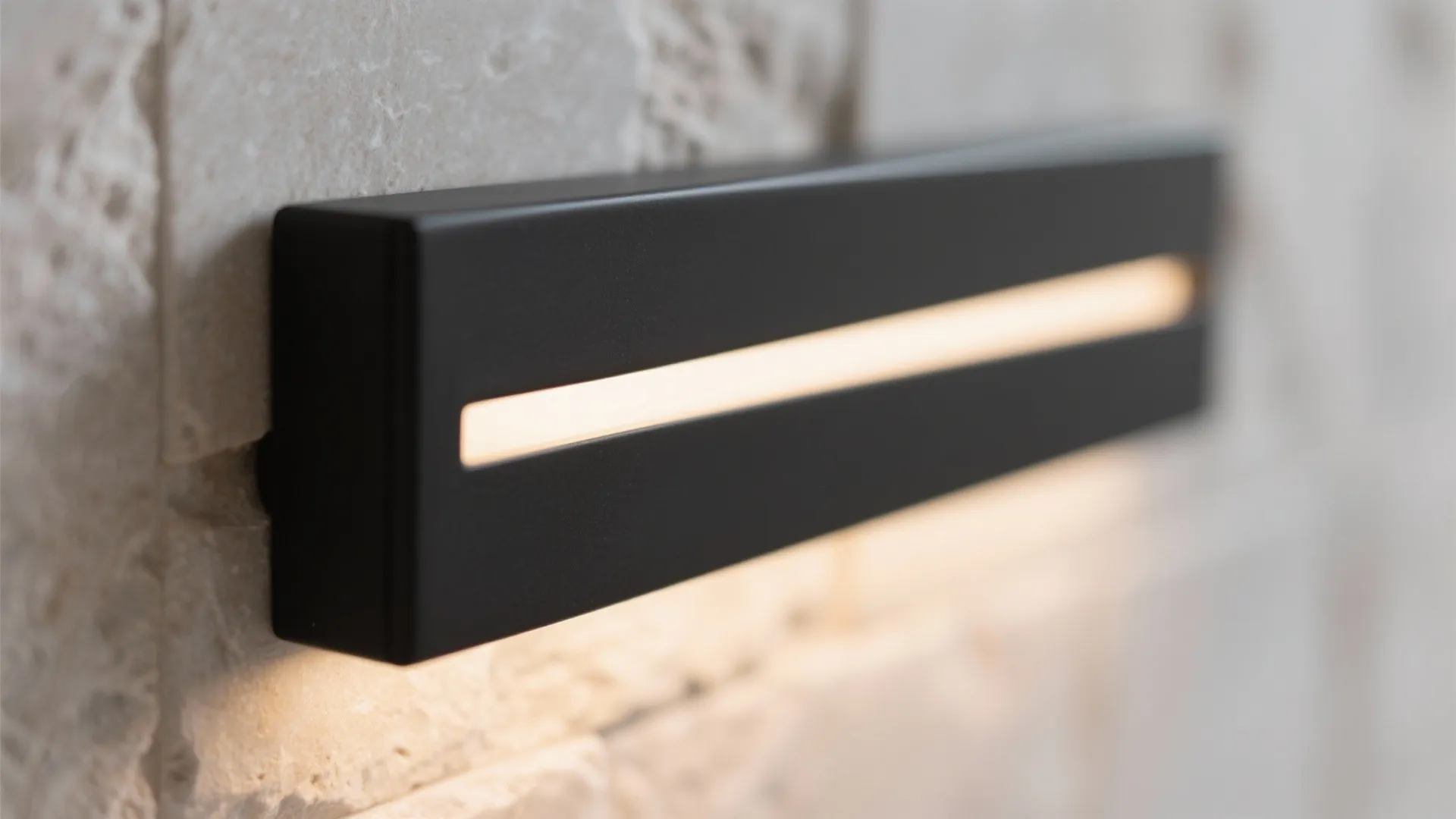 Modern black wall light with a warm glow mounted on a beige textured stone surface