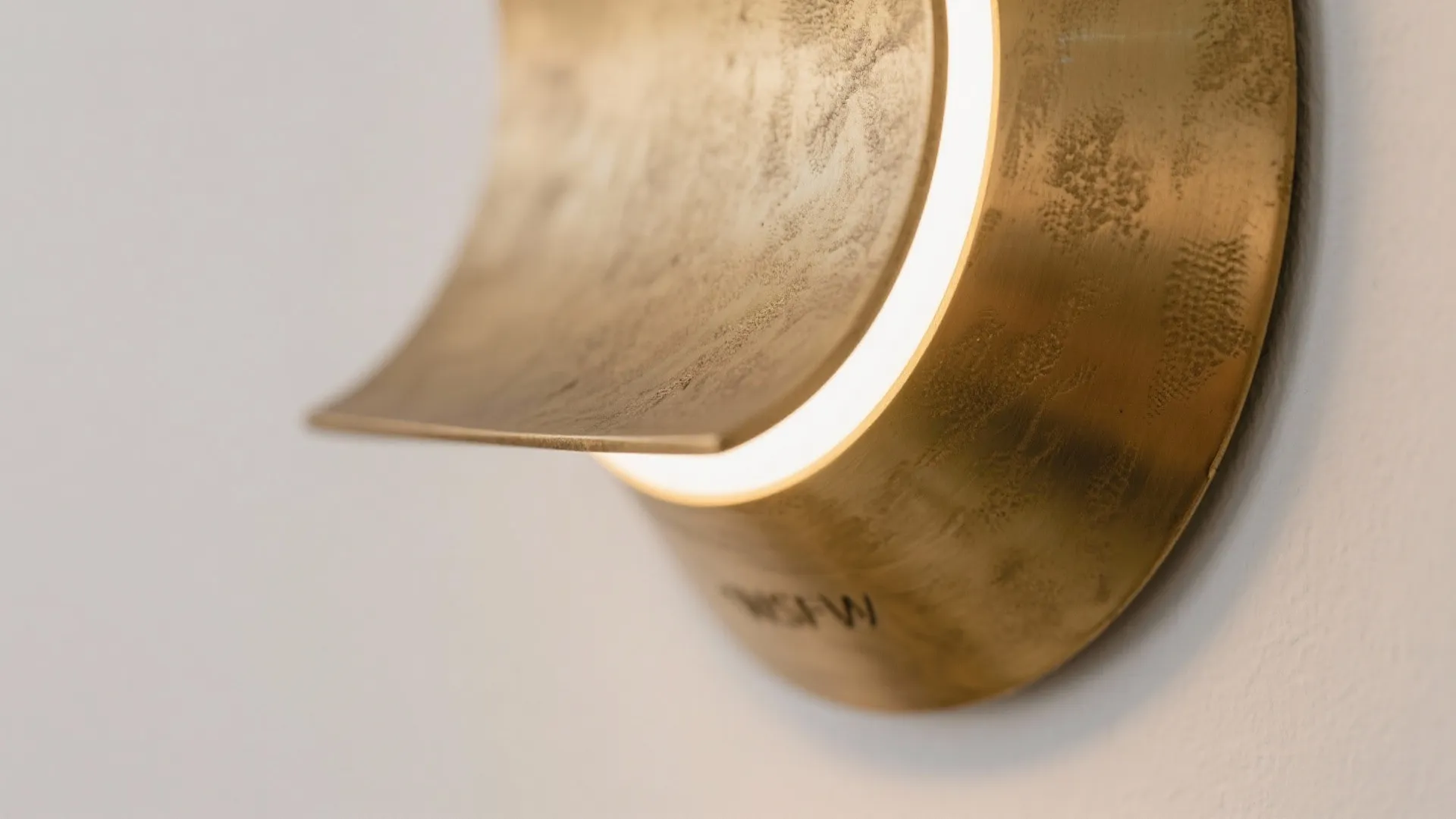 Close up view of a curved gold metal wall light with textured surface and warm light