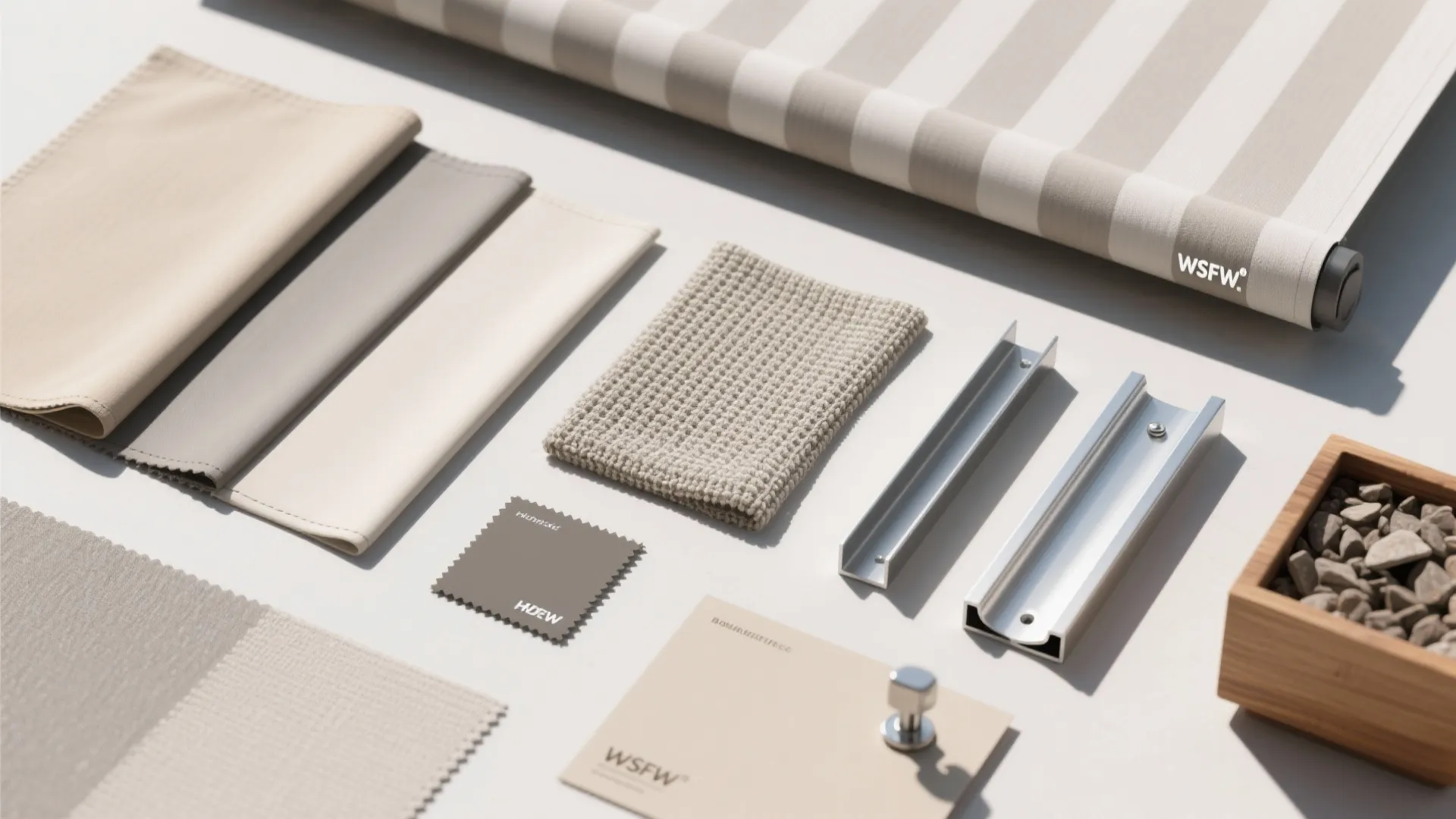 Collection of neutral window shade material samples with metal tracks and striped fabric on table