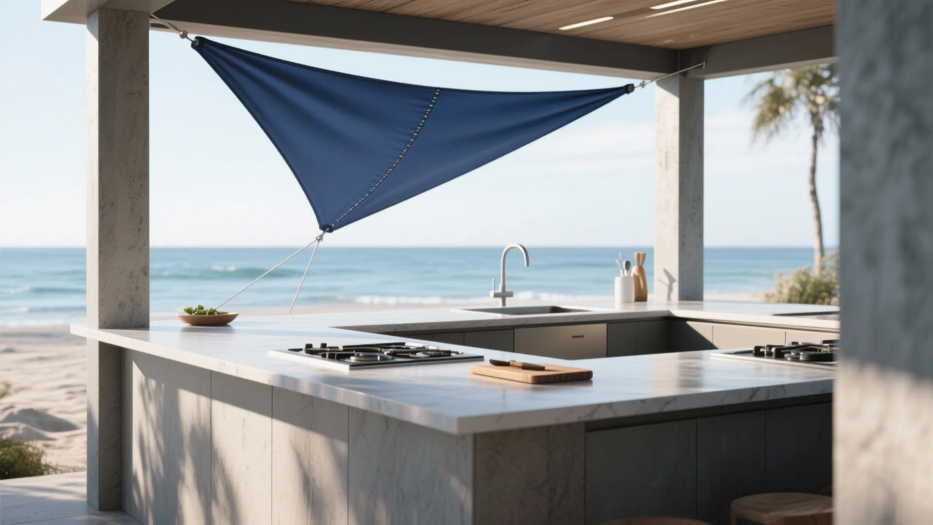 Modern outdoor kitchen with white counter and blue sun shade sail overlooking the blue ocean