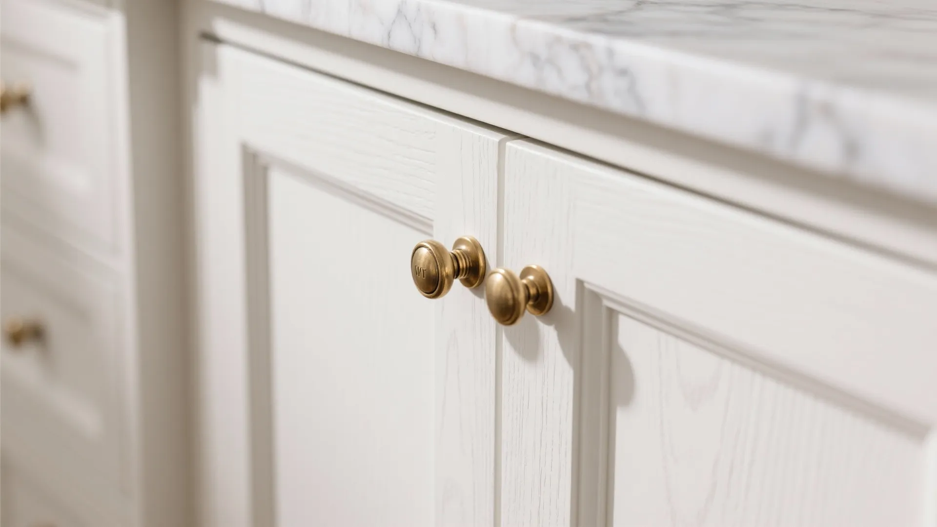 Close up of white bathroom cabinet with small round brass door knobs and marble countertop