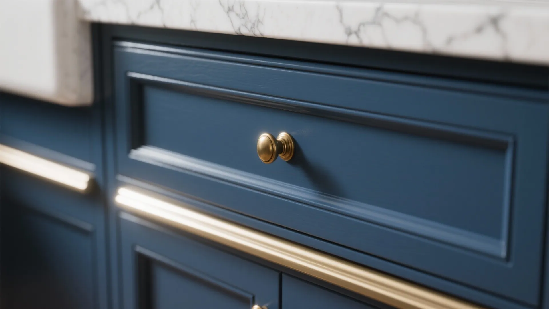 Detail of navy blue kitchen drawer with gold knob handle below white marble countertop and lighting