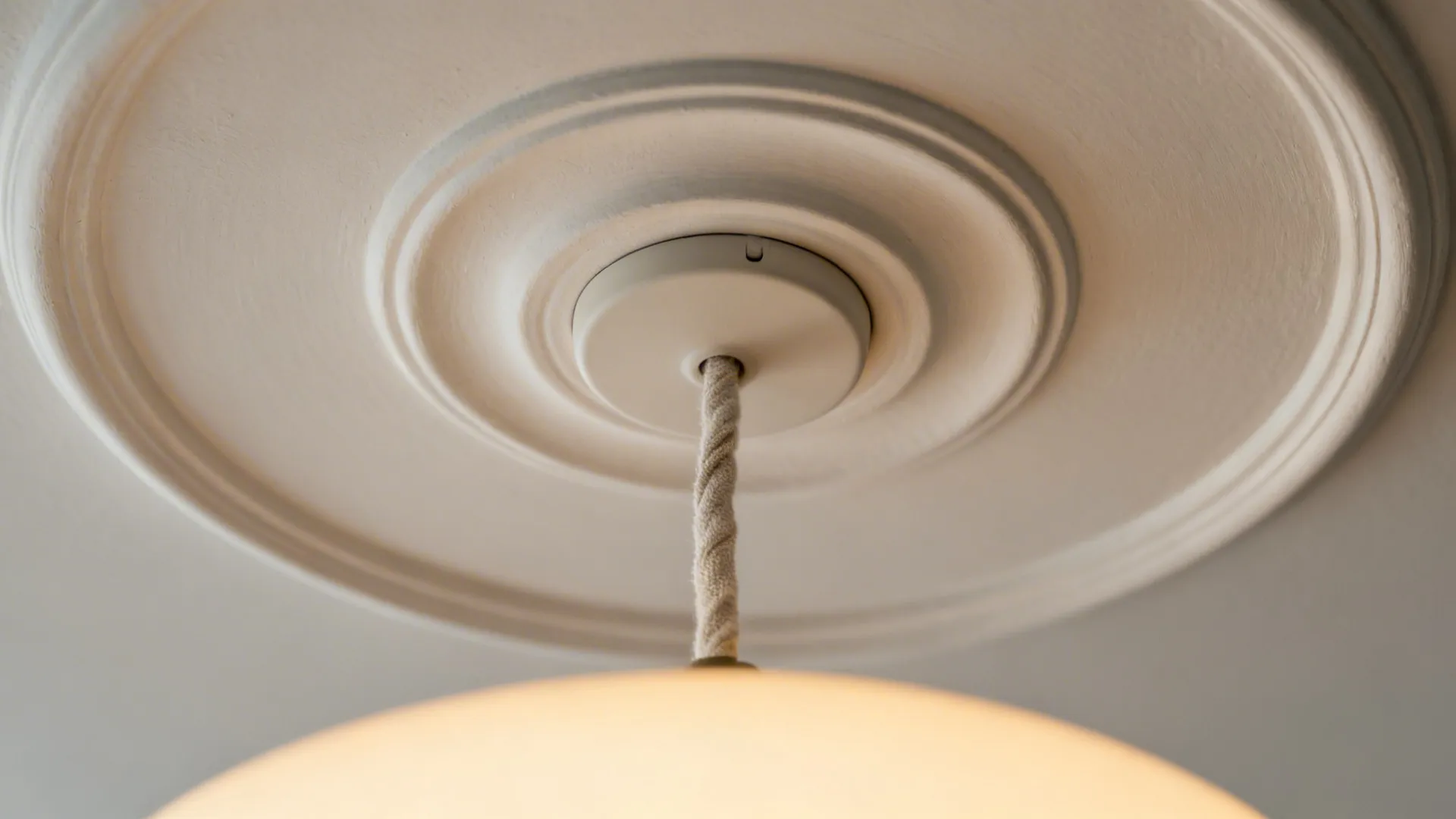 Close-up of a shallow plaster medallion with a slim pendant and fabric cord.