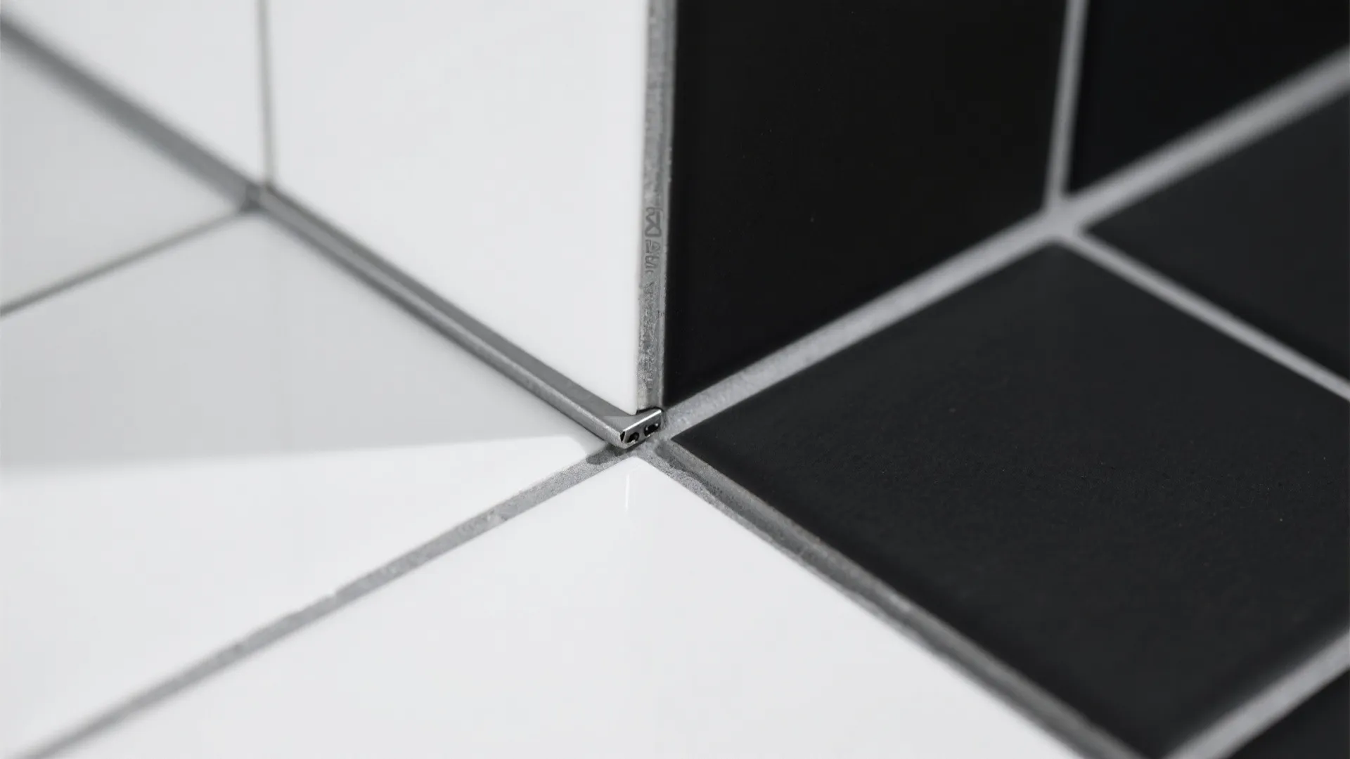 Close up of white and black wall tiles meeting at corner with silver metal edge
