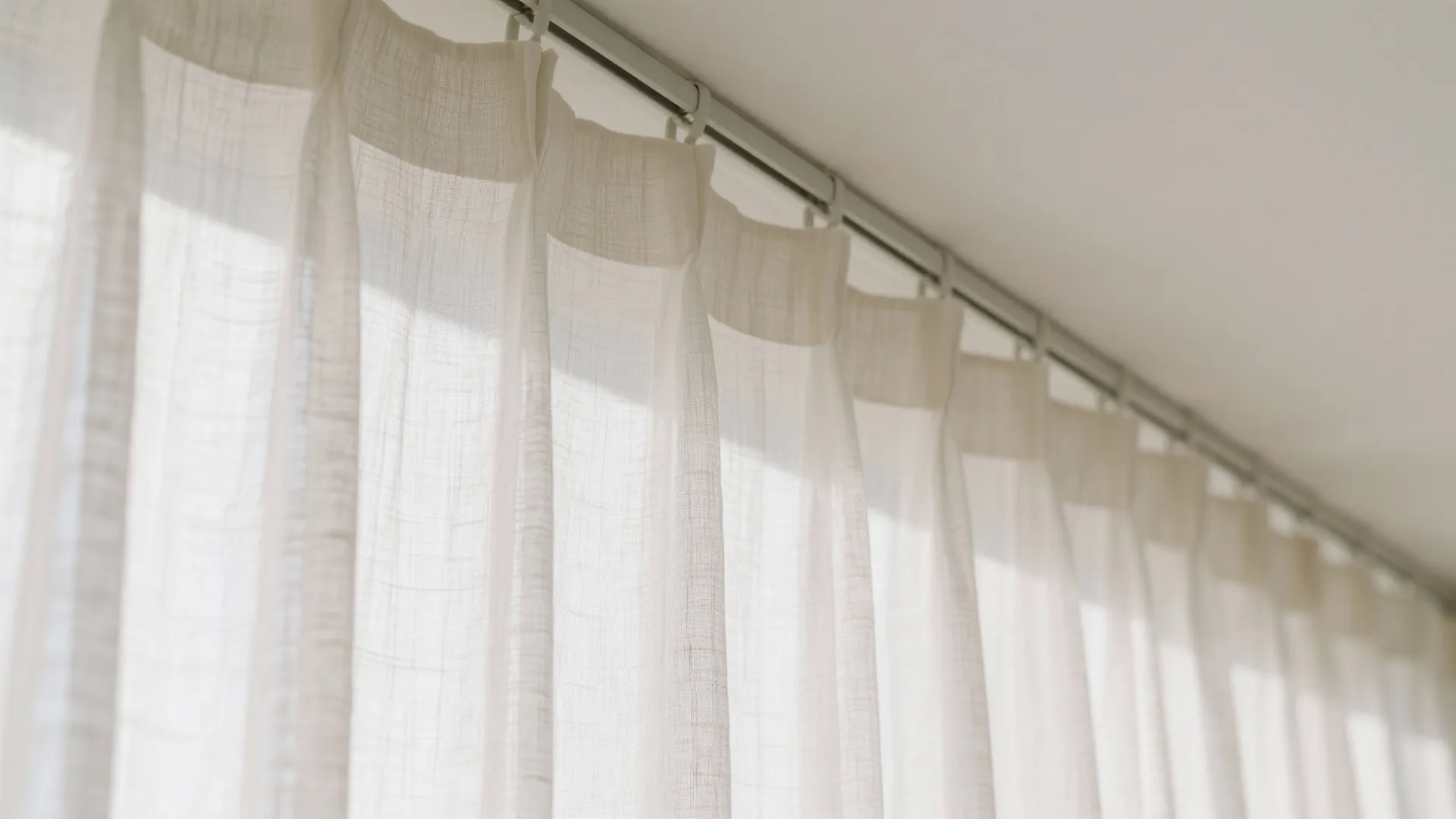 White sheer curtains hanging on a metal track attached to a clean and bright white ceiling