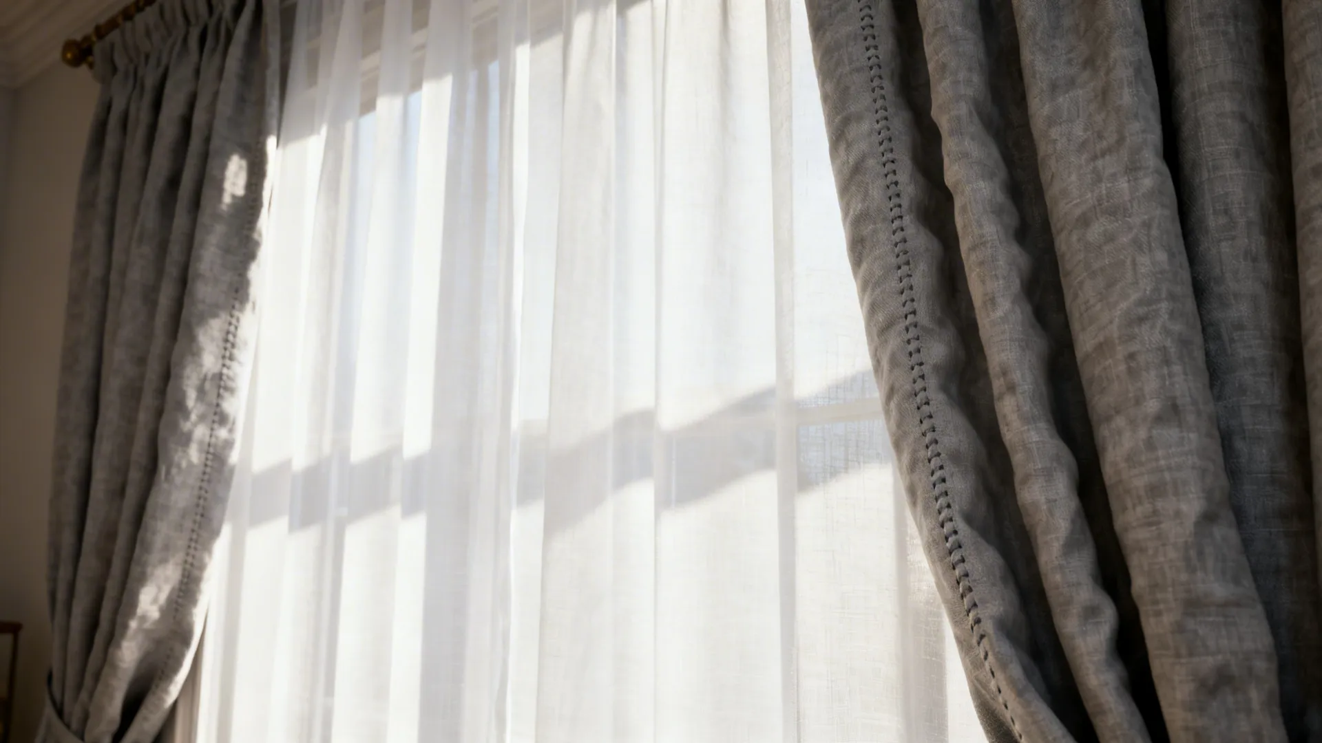 Close-up of sheer white panels layered with grey linen drapes showing texture and soft daylight.