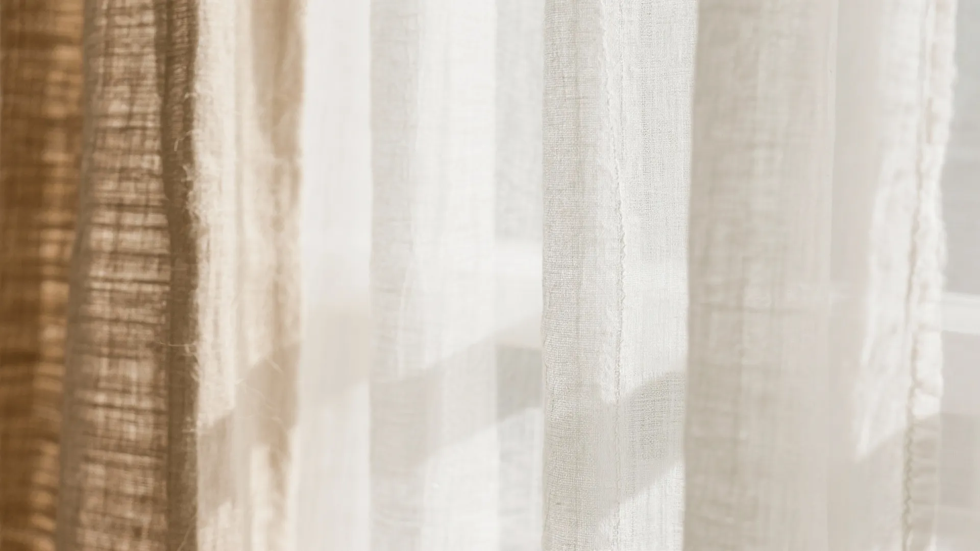 Macro view showing the delicate weave of sheer fabric layered over textured linen in warm beige.
