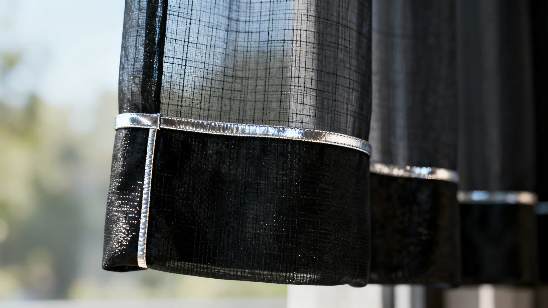 Close up of black sheer curtain fabric with a decorative silver metal trim at bottom