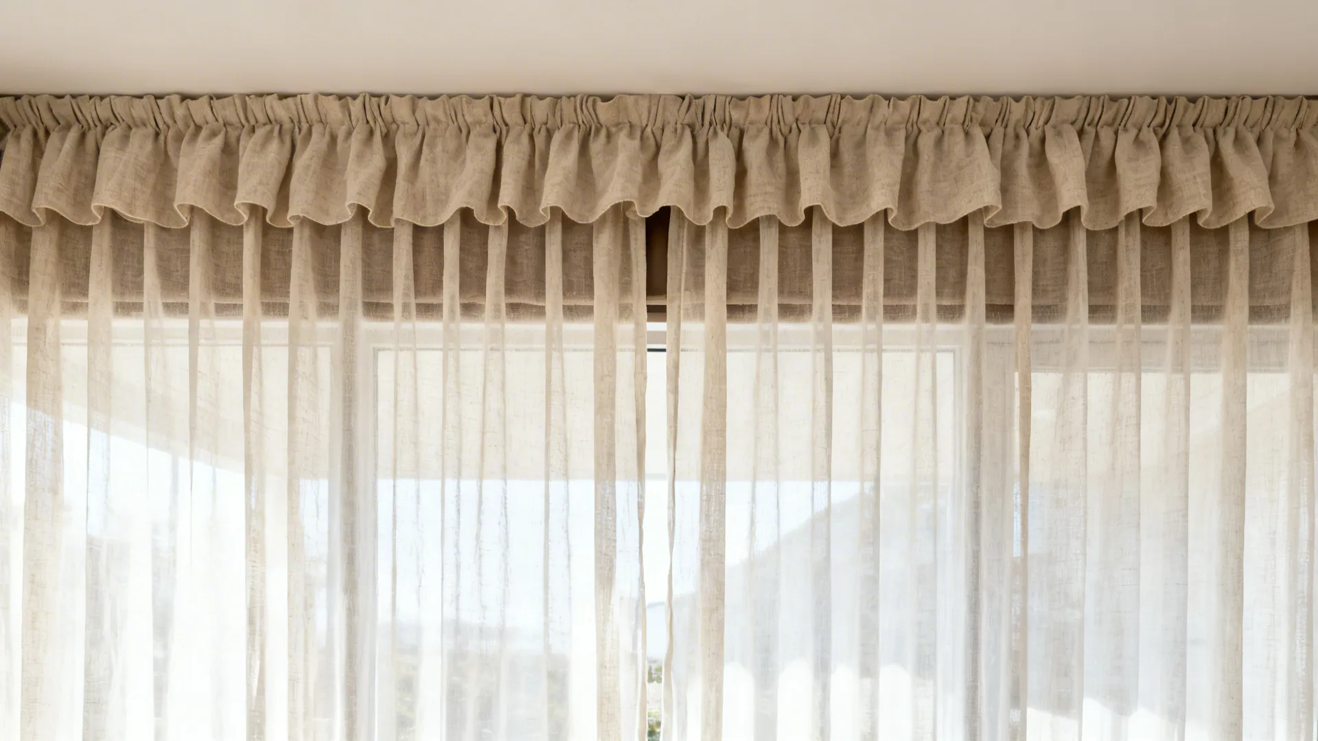 Light beige ruffled curtain hanging over sheer white fabric across a bright window with natural light