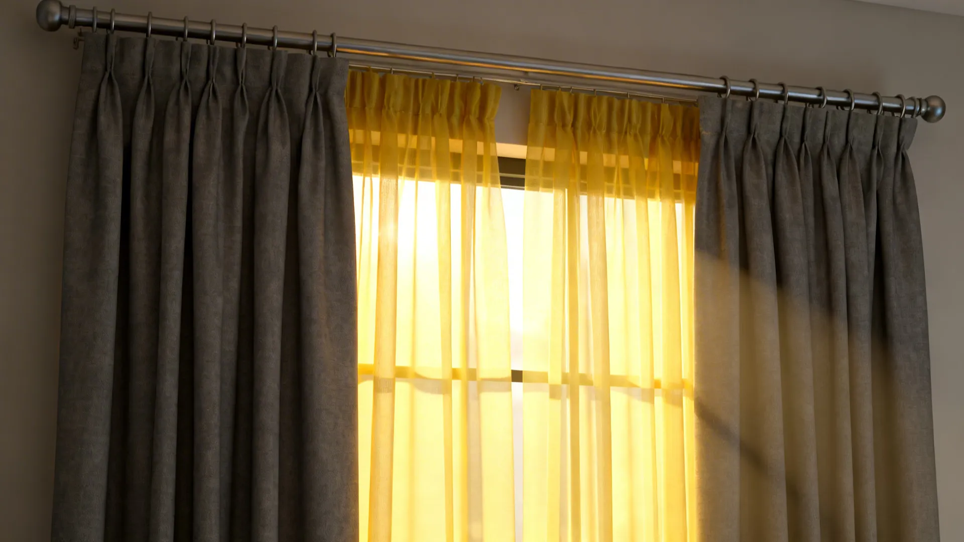 Layered sheer yellow veil behind grey blackout panels with two-rod installation and warm morning glow.