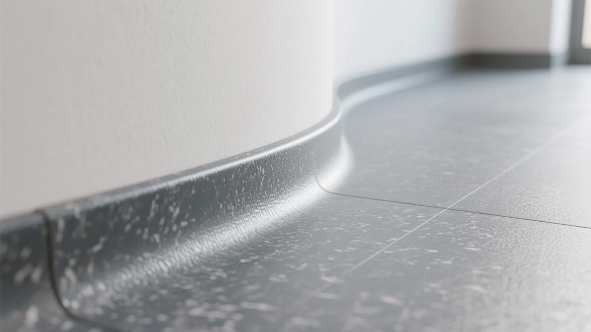Close up view of curved grey vinyl flooring meeting a white wall in a room