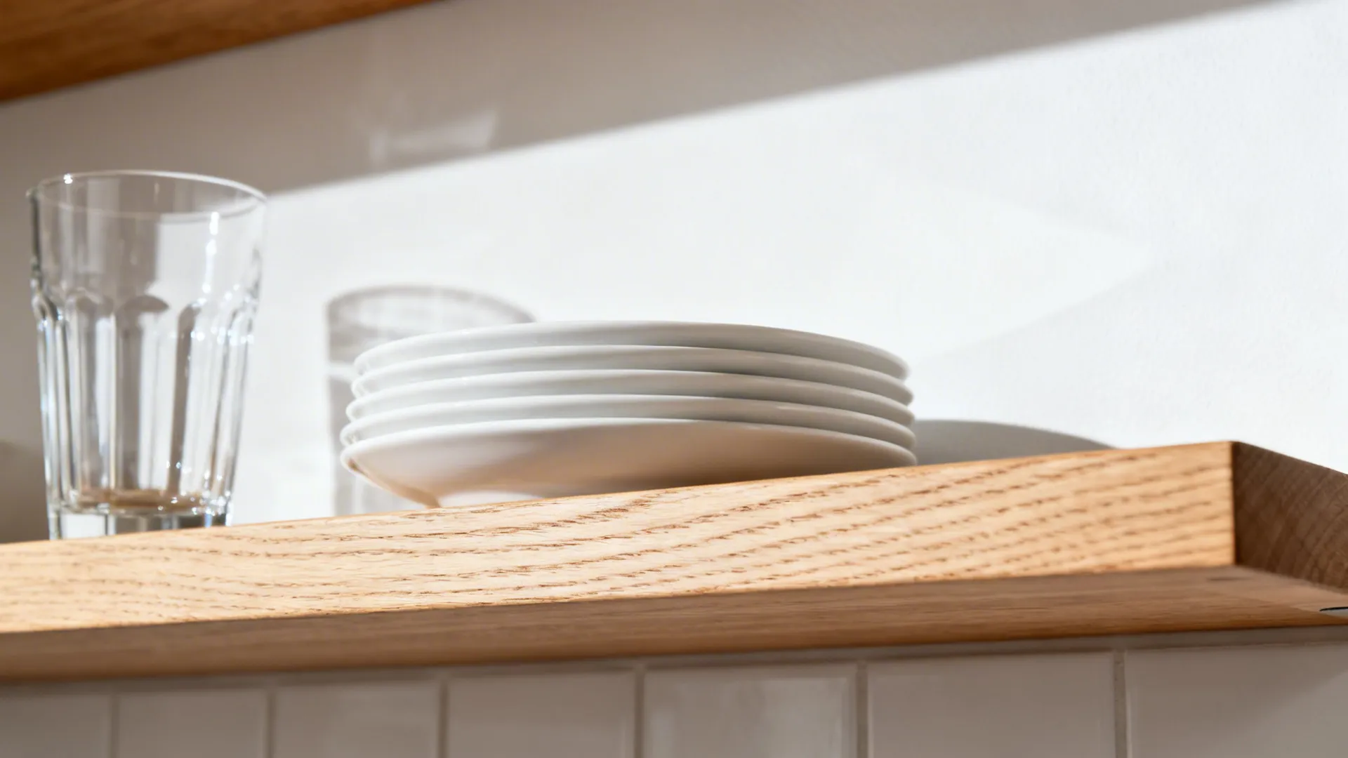 Close up of wooden wall shelf with stack of white plates and two glass cups