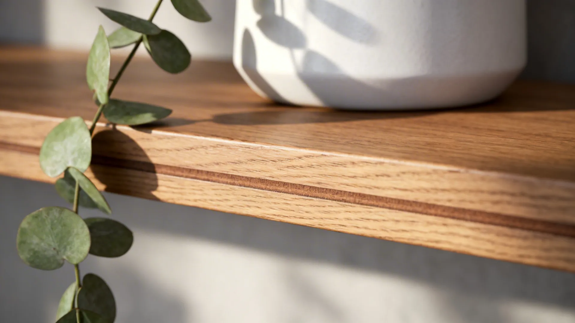 Macro of oak shelf edge with plant leaf and matte ceramic texture.
