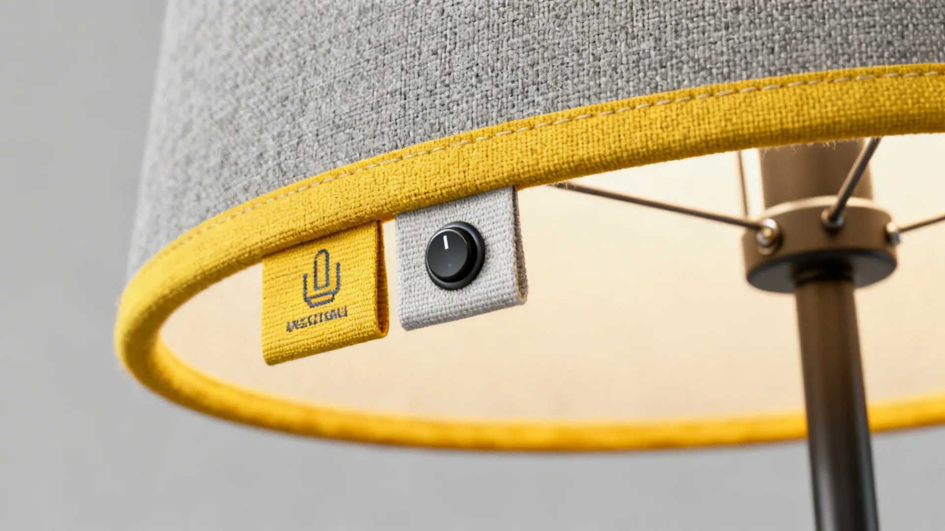 Close up of grey fabric lamp shade with yellow trim showing black power button and label