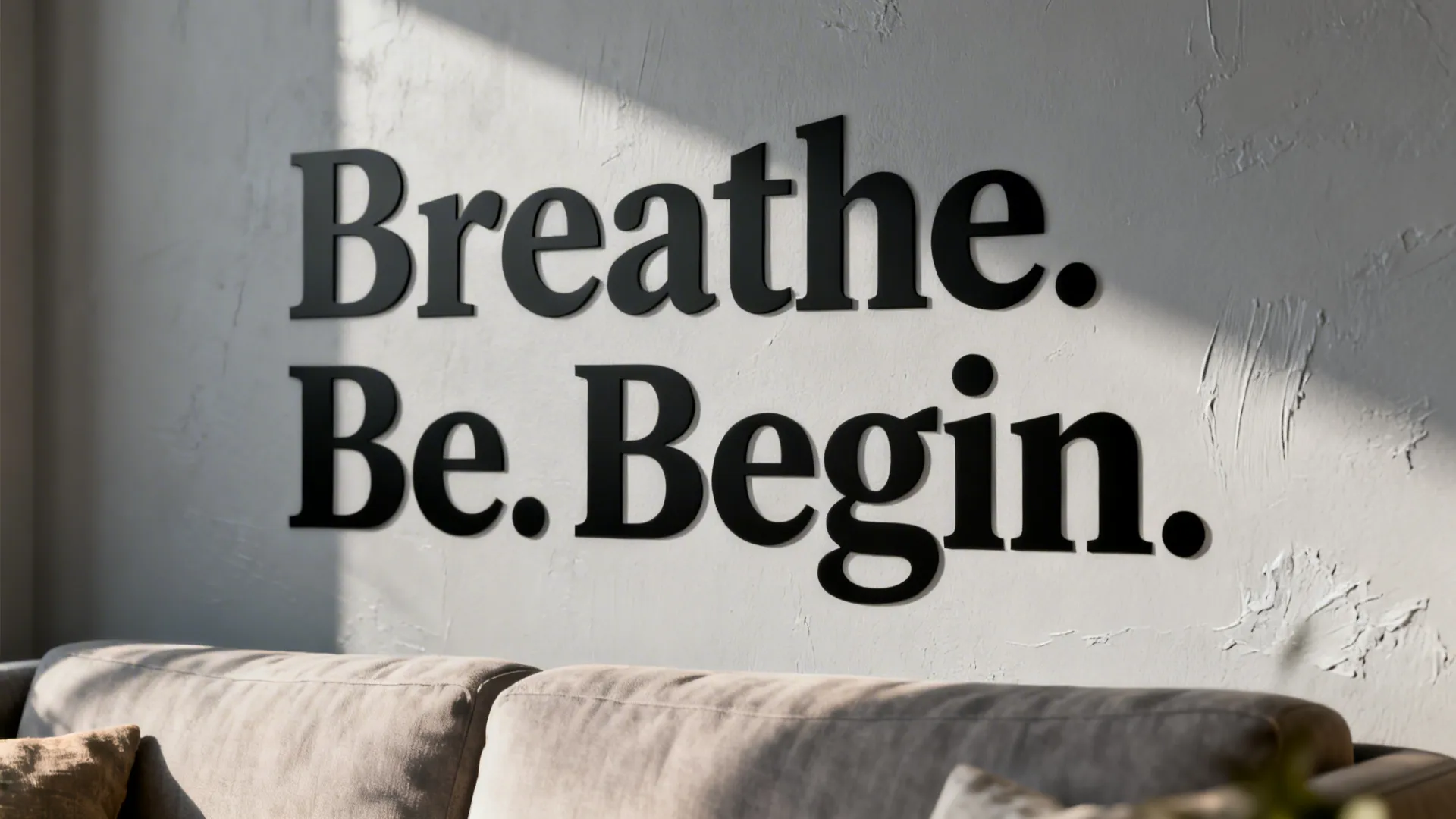 Black wall letters saying Breathe Be Begin on white textured background with sunlight above sofa