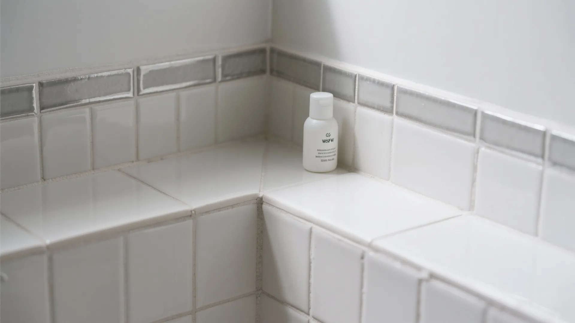 Close up view of white bathroom wall tiles with a small shelf holding one bottle