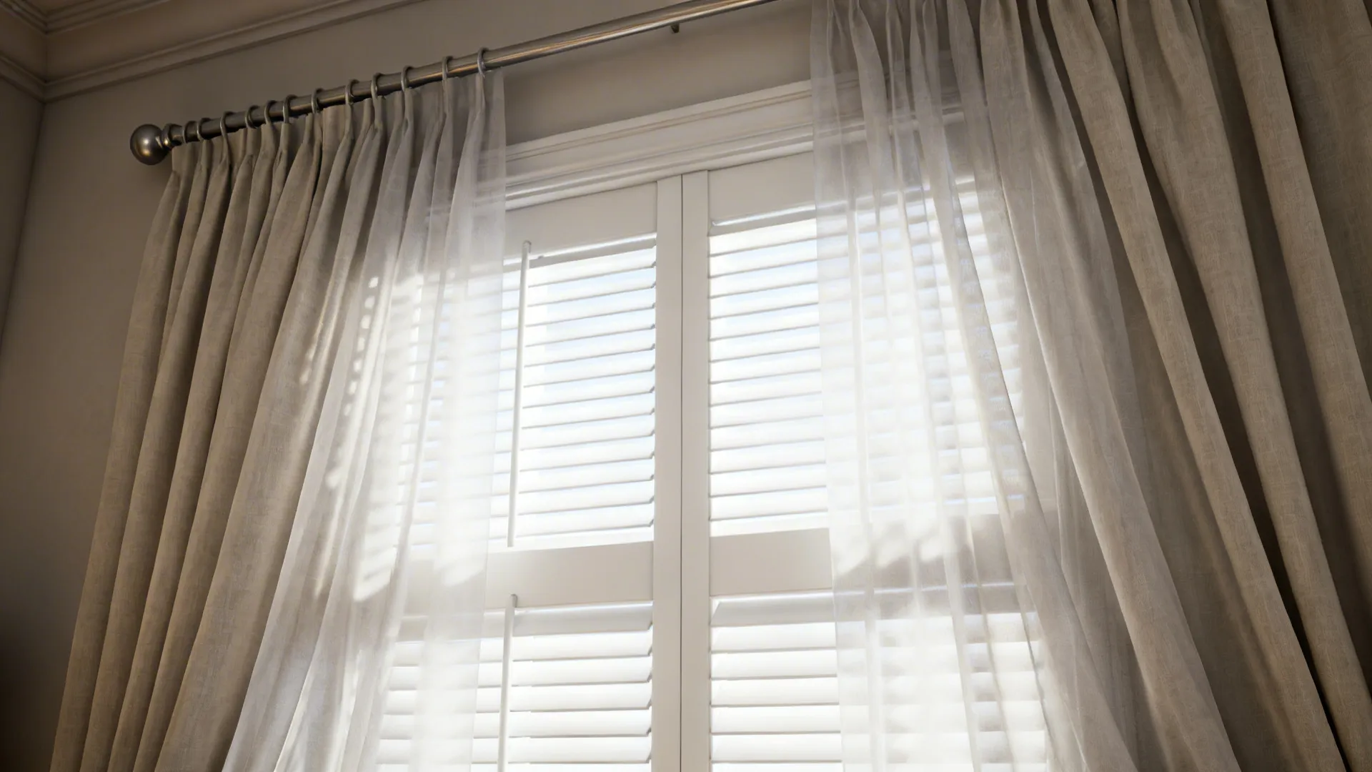 Layered window treatment with plantation shutters and flowing sheer curtains, showing fabric texture and hardware
